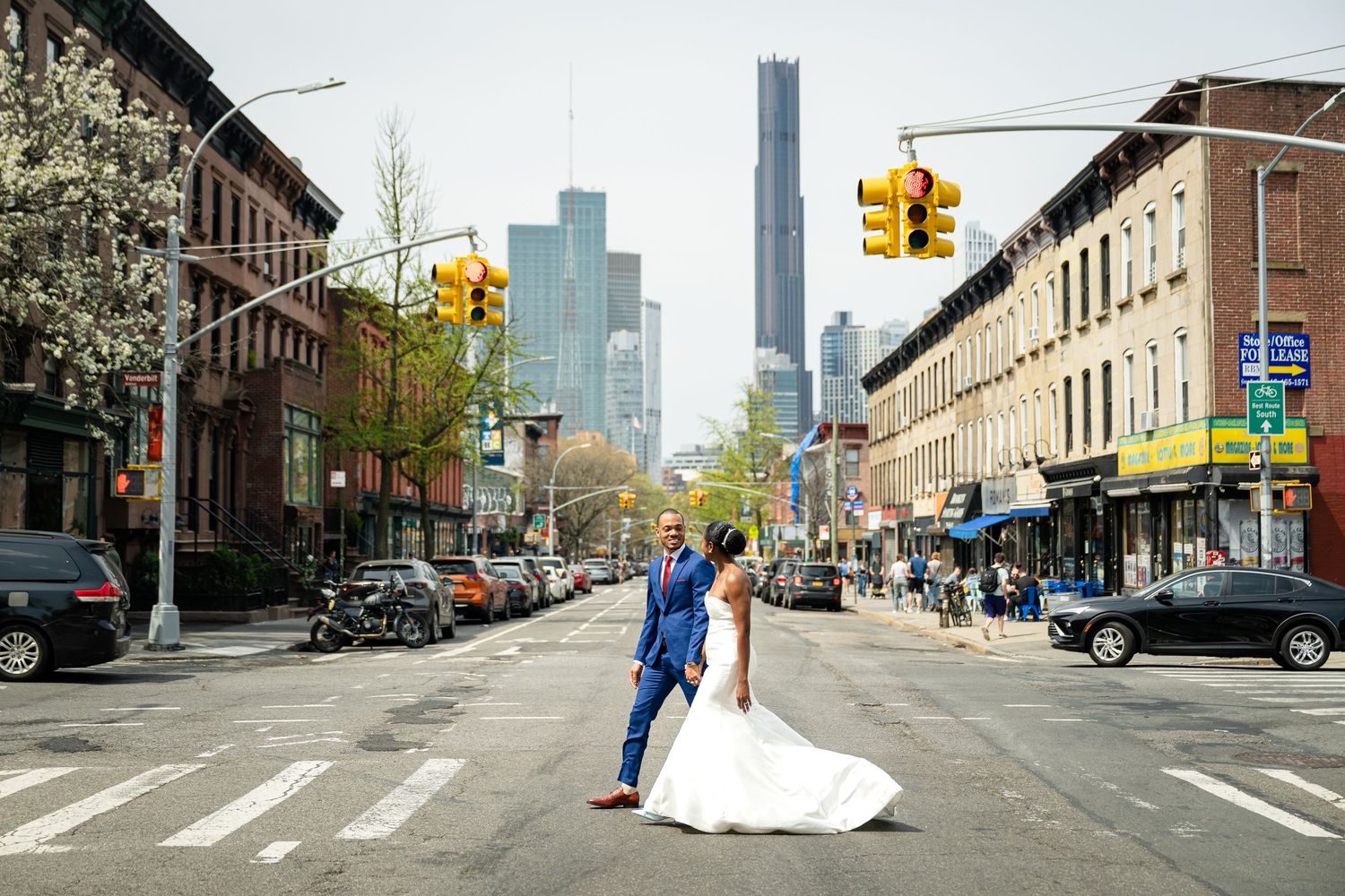 Wedding couple in blue suit and white dress pose on a New York City street with skyscrapers in background.