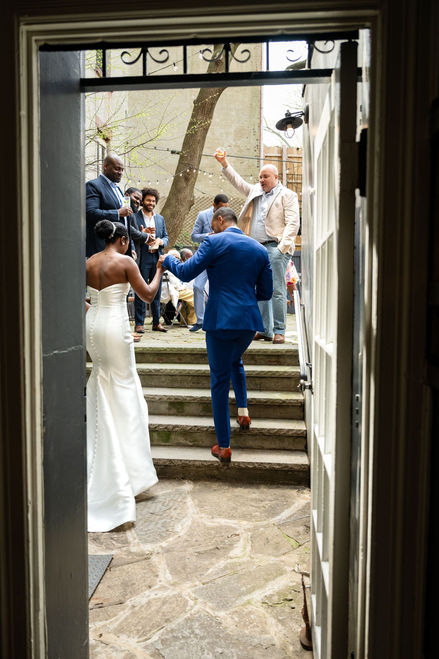 Wedding guests gathering on stone steps viewed through an ornate doorframe.