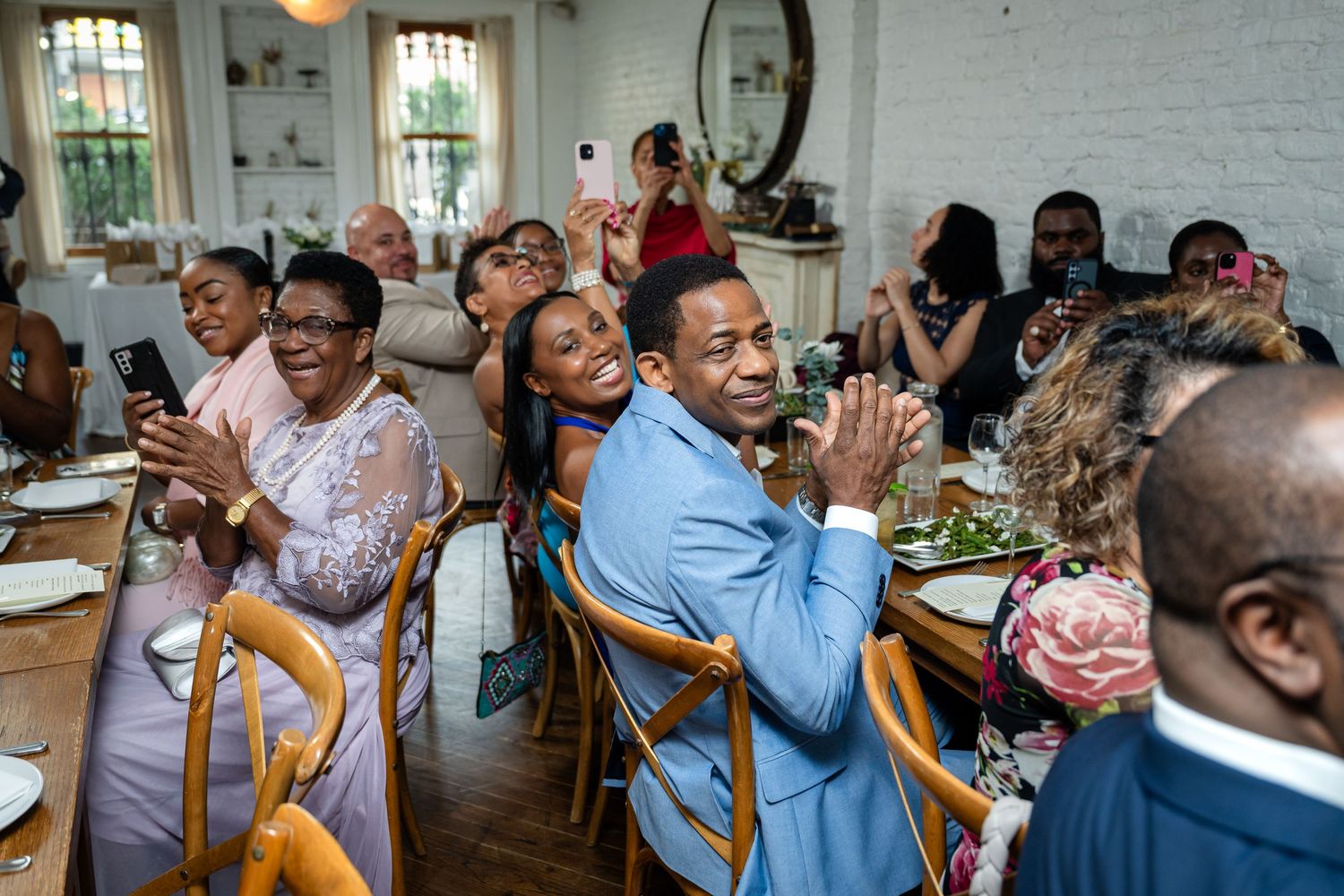 Wedding reception guests laugh and celebrate at indoor dining tables.