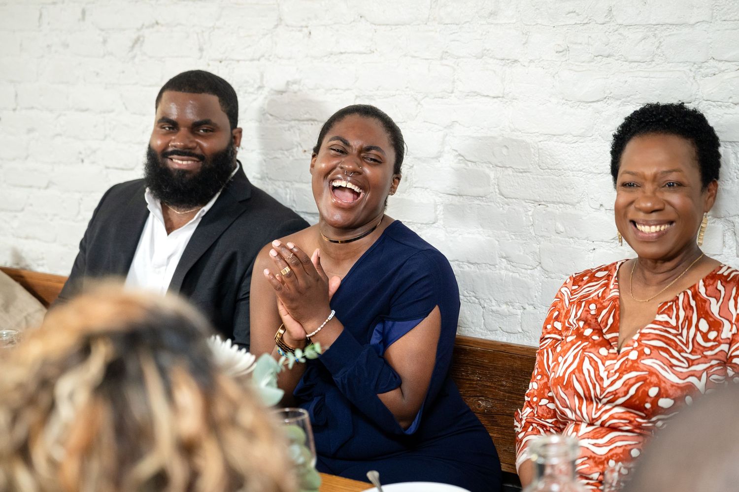 A group of wedding guests share joyful laughter while seated together at a celebration.