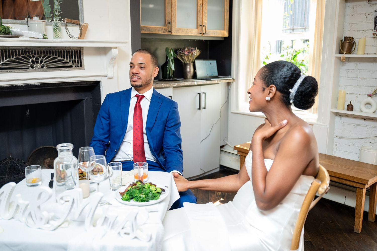 A newlywed couple enjoying their reception meal at an intimate indoor setting.