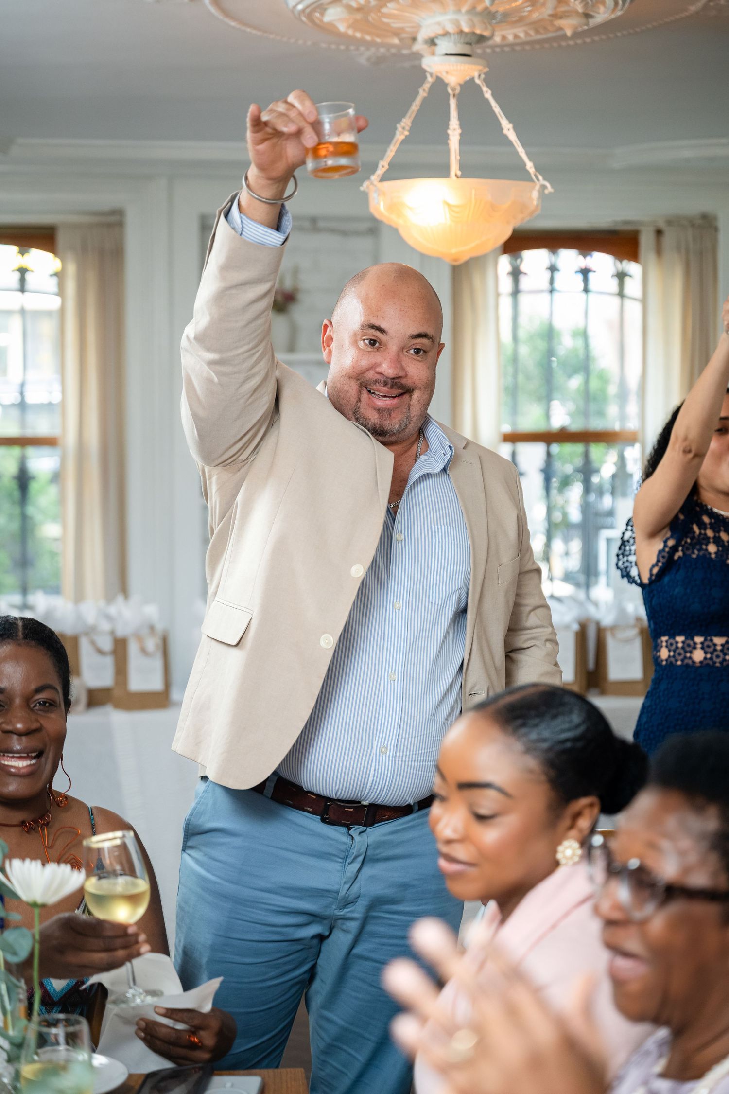 A celebratory gathering in an elegant dining room with chandelier lighting as someone makes a toast with drinks.