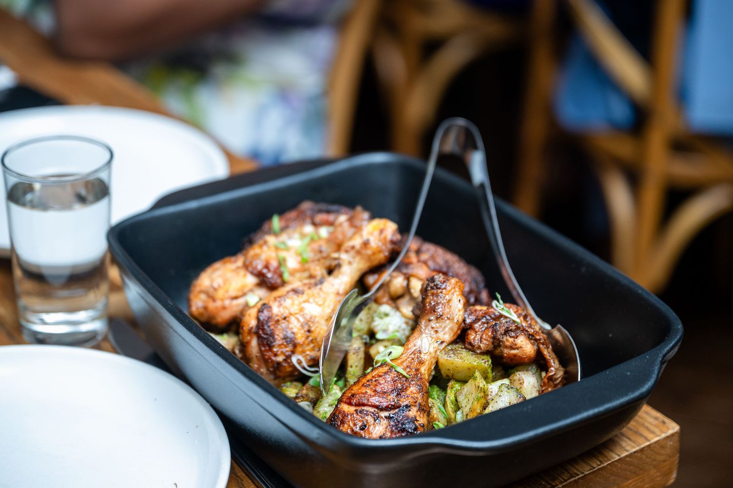 Grilled chicken with vegetables served in a black pan with garnish and table settings.