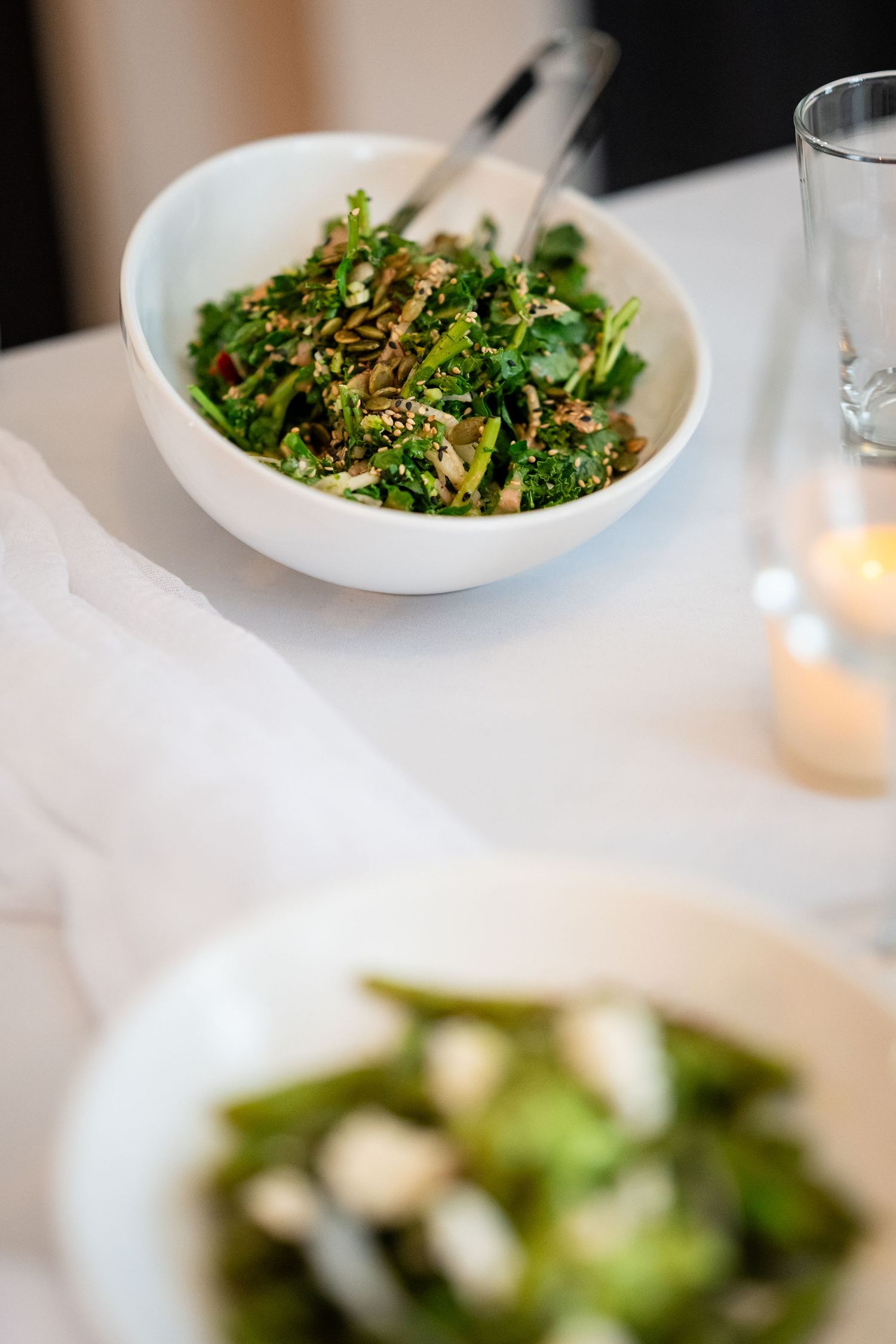 Fresh green salad topped with sesame seeds served in a white bowl on an elegant table setting.