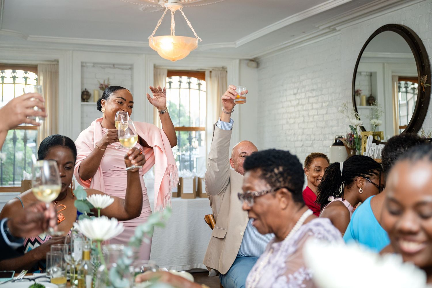 Joyful wedding guests raising their hands in celebration during reception dinner.