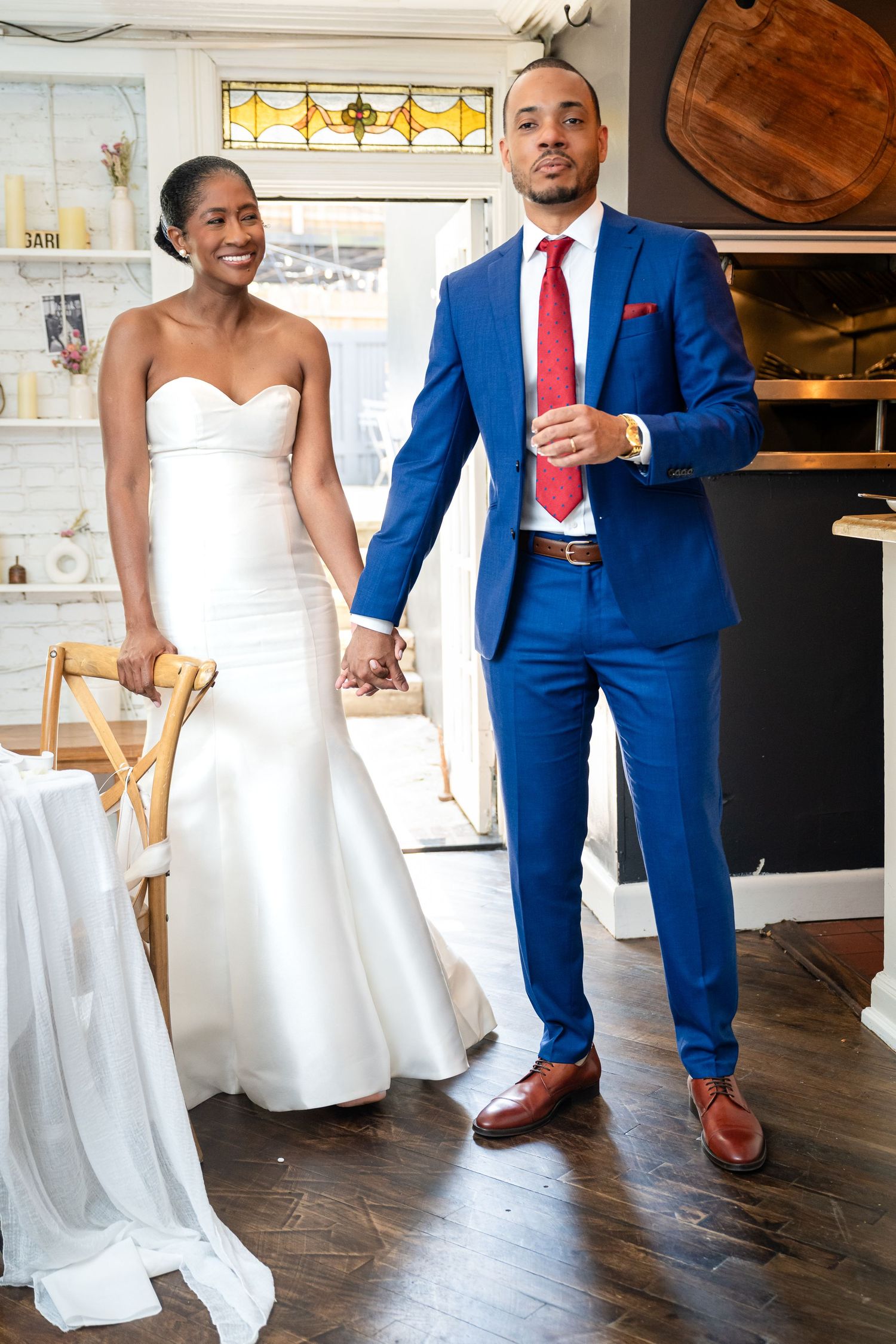 A couple in wedding attire standing together, featuring a blue suit and white strapless gown.