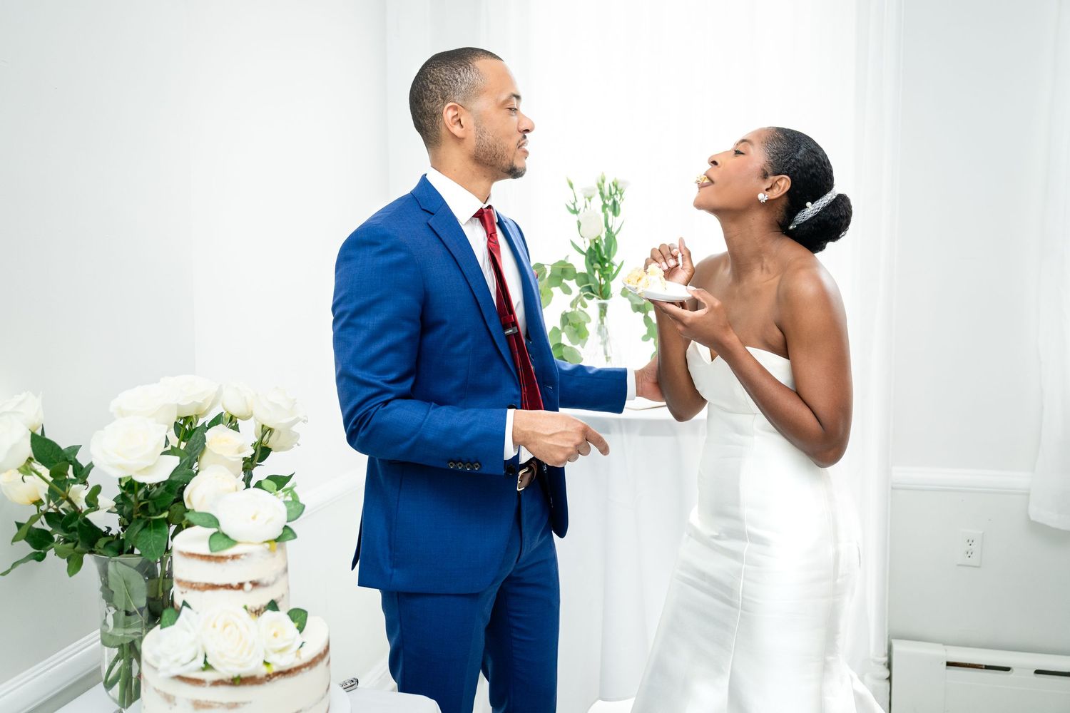 A couple in wedding attire sharing a playful moment next to their wedding cake.