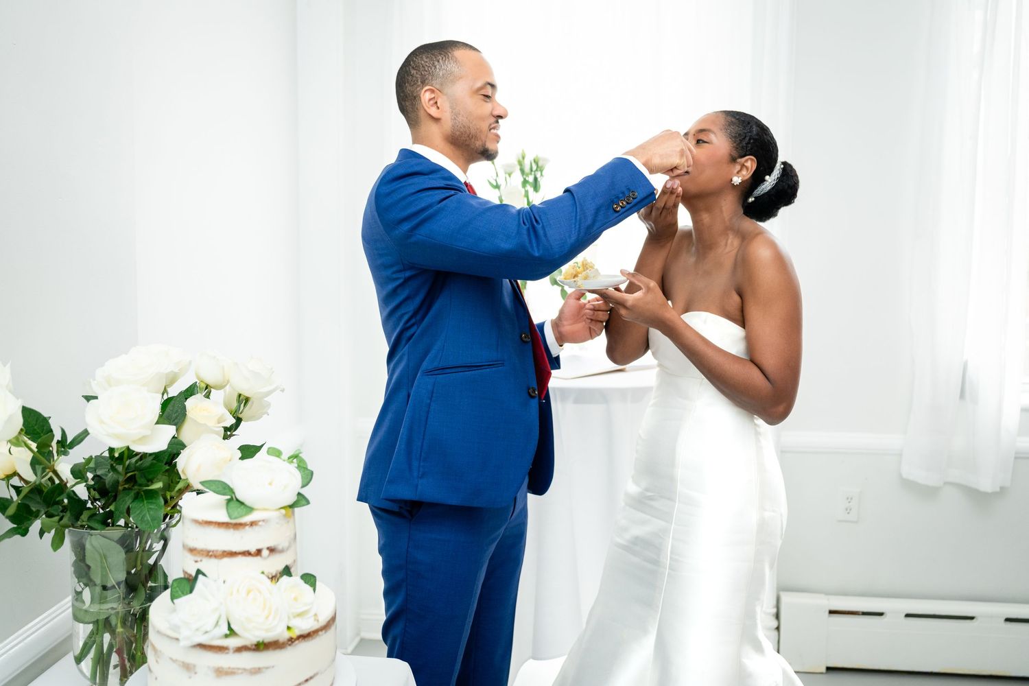 Newlyweds playfully feed each other cake during their wedding reception celebration.