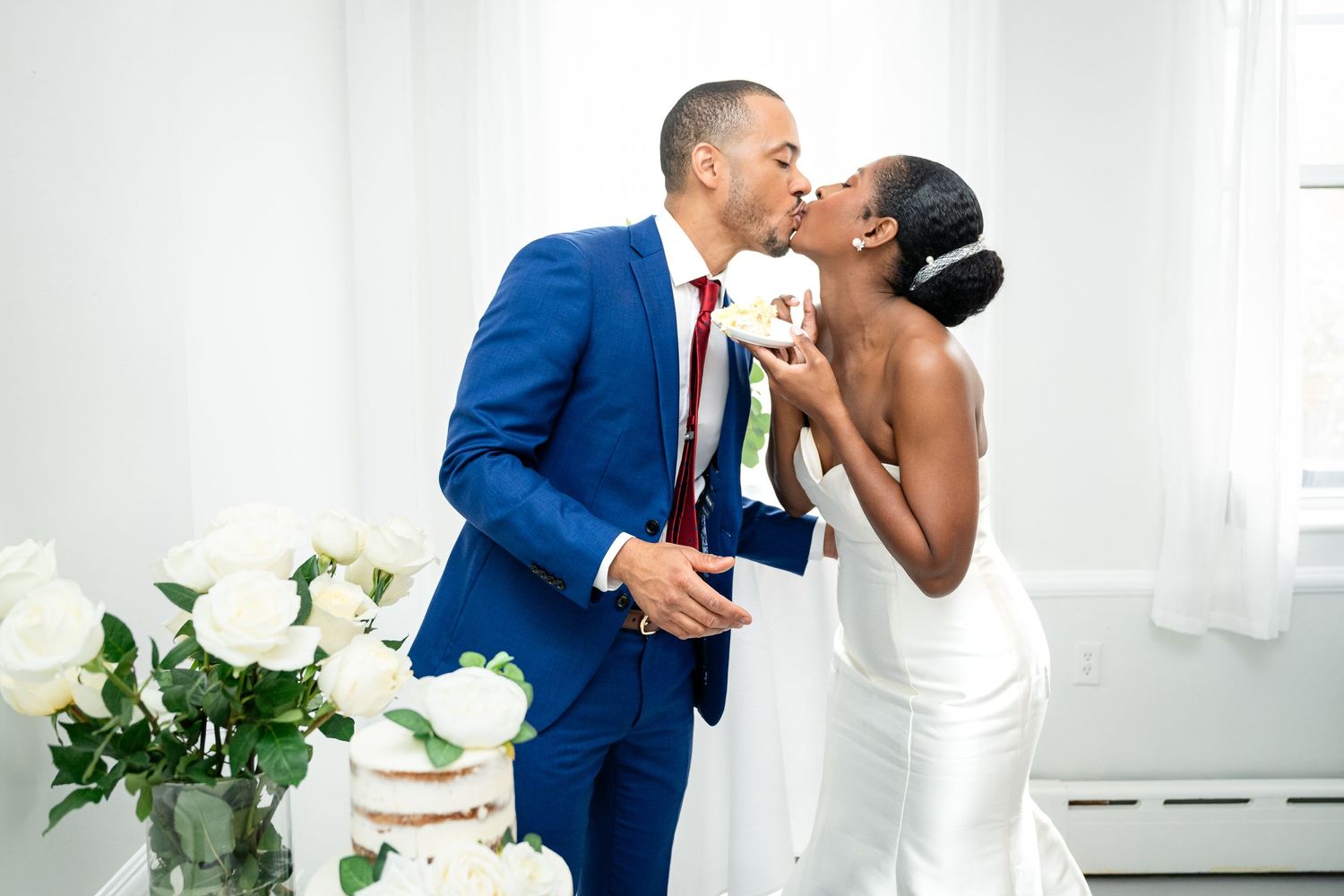 A couple share an intimate moment near white floral arrangements in a bright indoor setting.