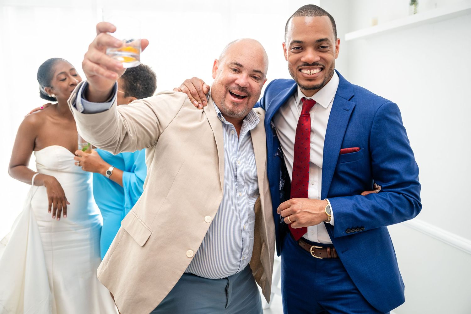 Wedding guests celebrate with drinks at a joyous reception in an elegant white venue.