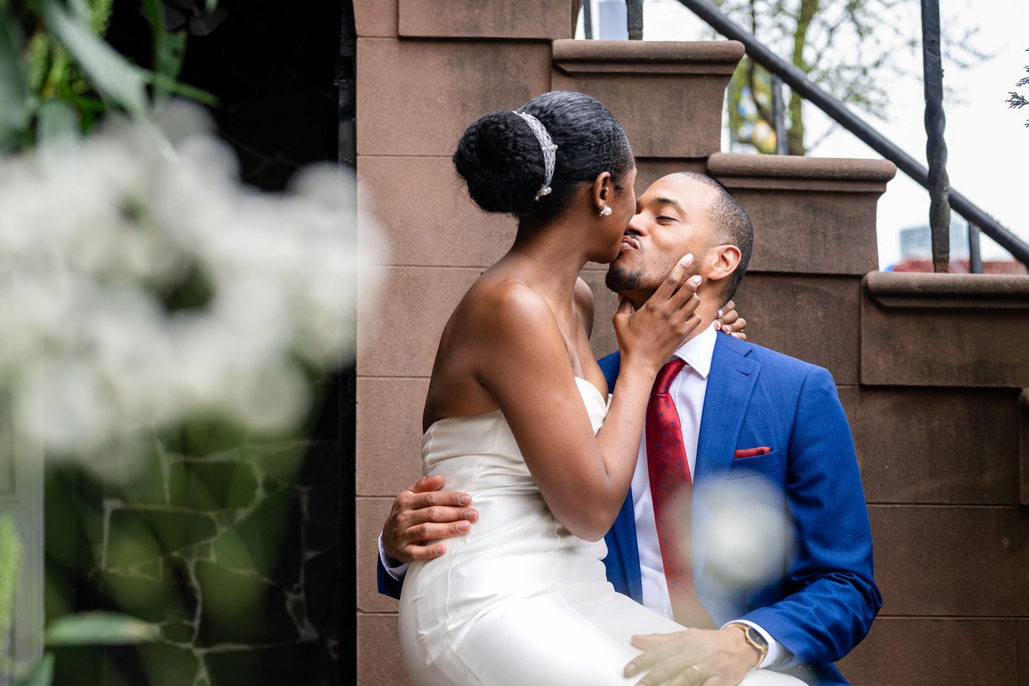 A romantic moment captured on brownstone steps with soft focus flowers in the foreground.