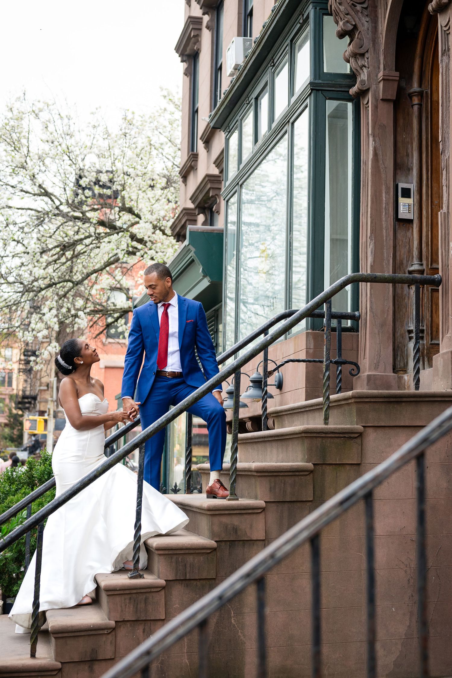 A couple poses romantically on brownstone steps while wearing wedding attire.