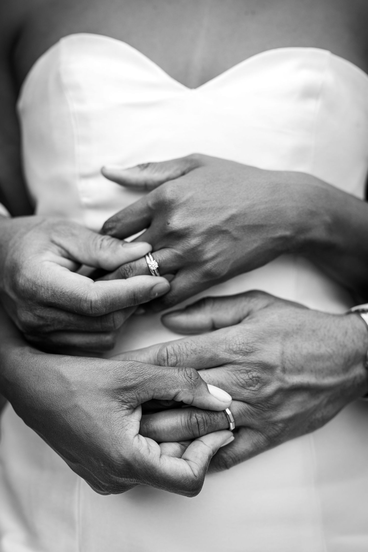Close-up black and white photo of hands with wedding rings against a white dress.