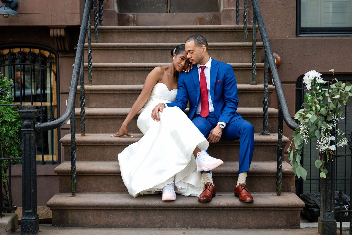 A newlywed couple sits together on brownstone steps in formal wedding attire.
