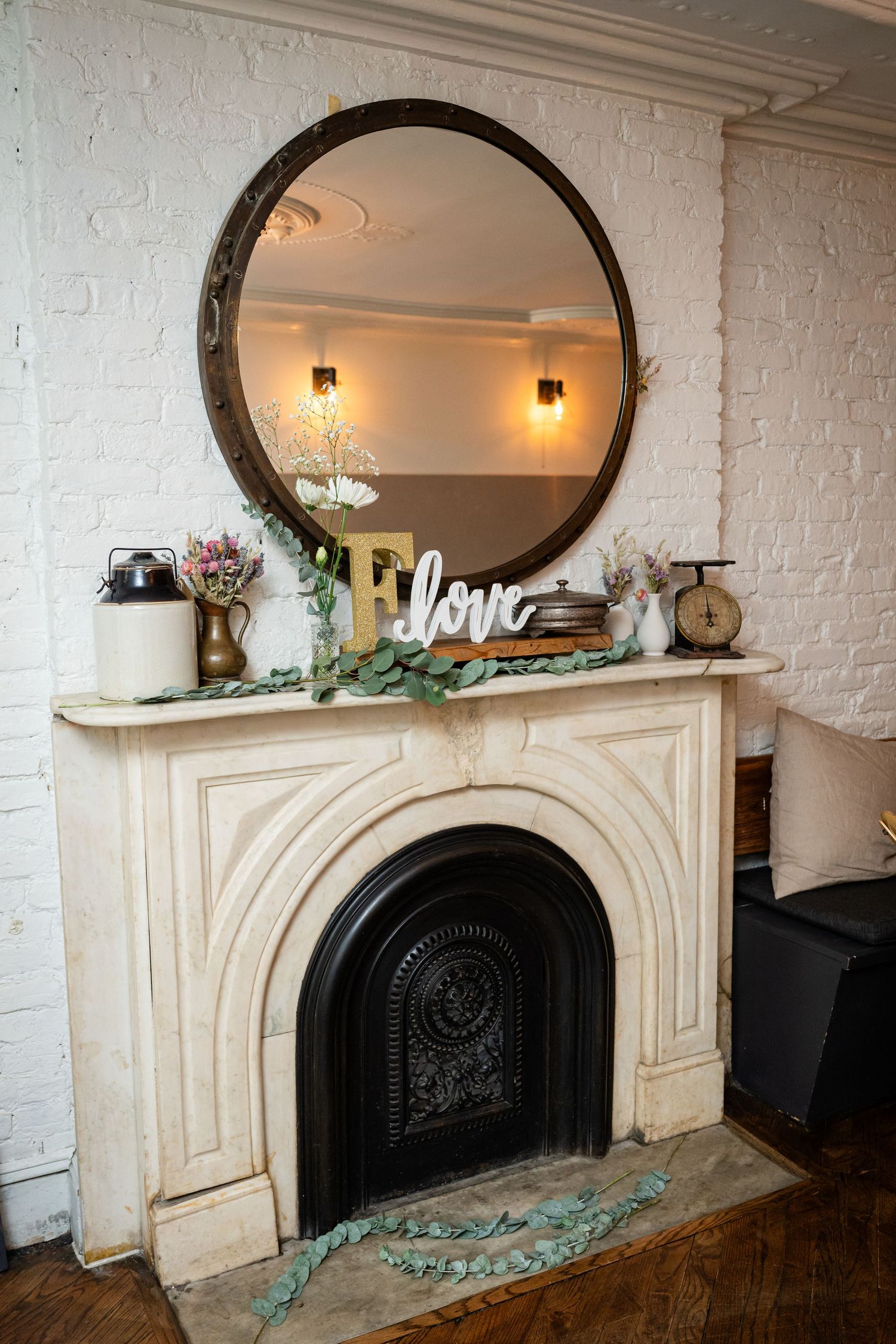 Elegant marble fireplace mantel with round mirror, love sign, and decorative accents against white brick wall.