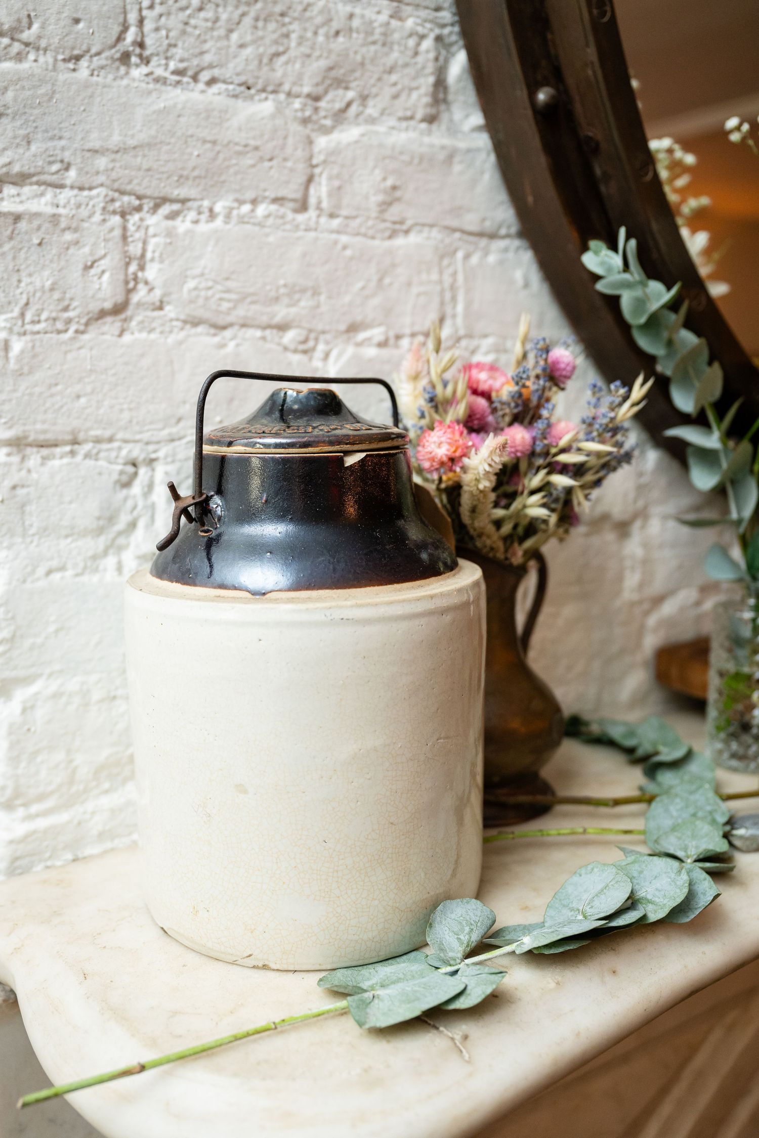 Vintage ceramic jug and dried flower arrangement against whitewashed brick wall.