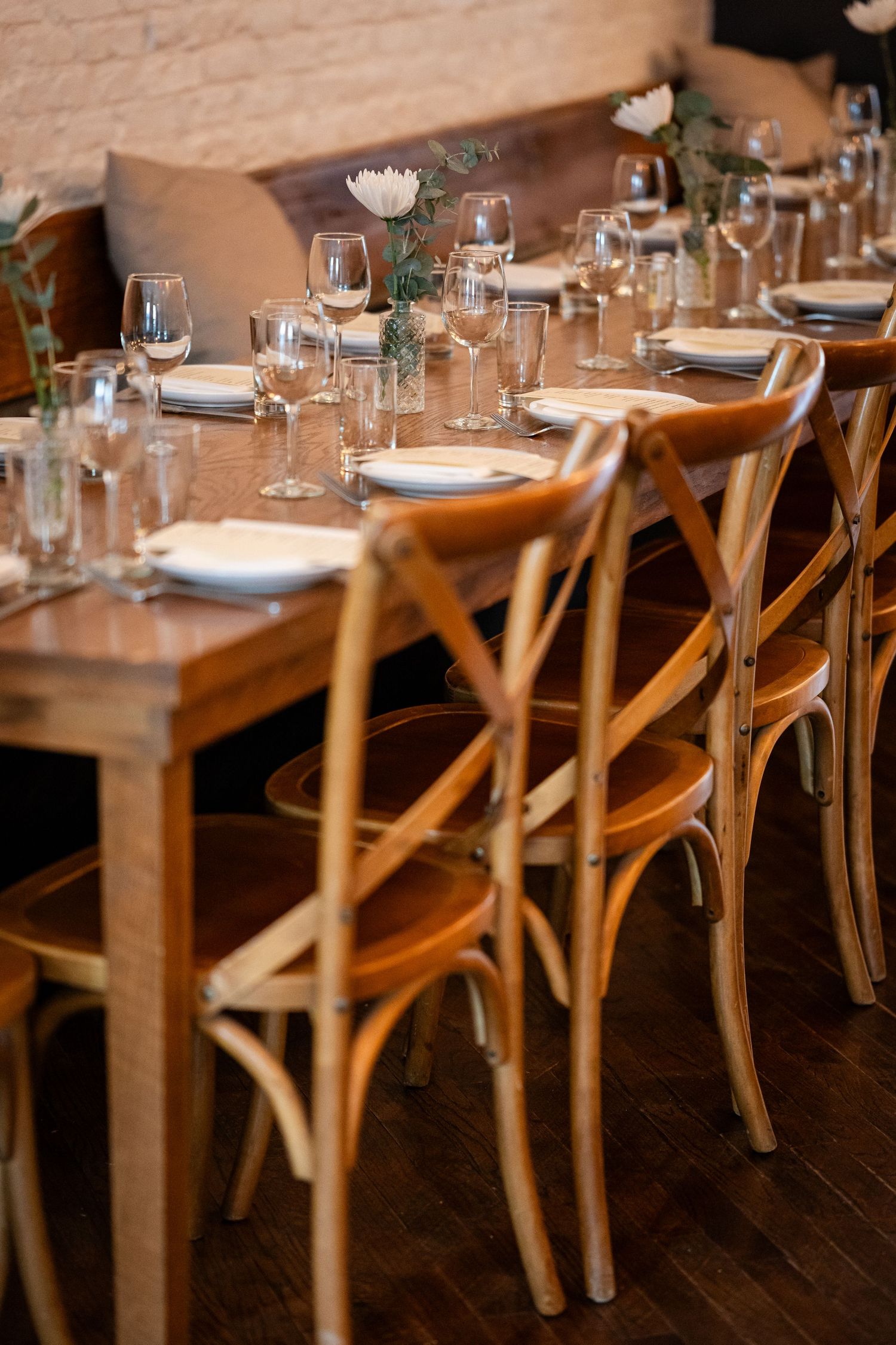 Elegant table setting with wooden crossback chairs and wine glasses in rustic dining room.