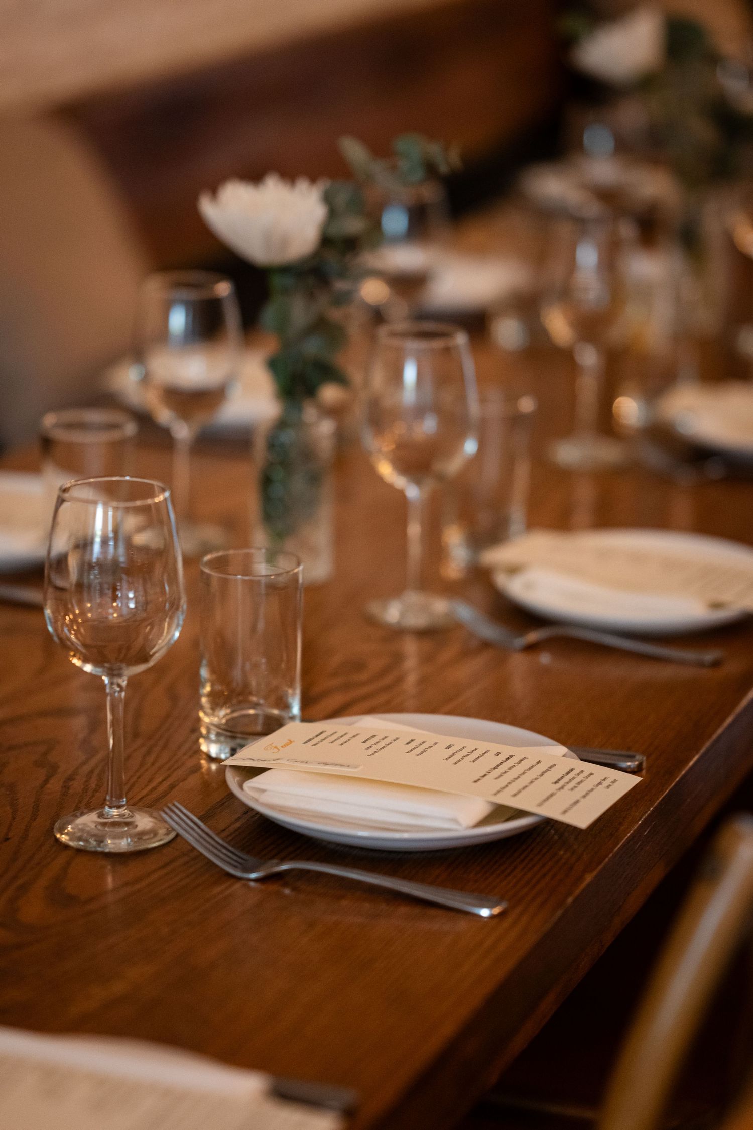 An elegant wedding reception table setting with wine glasses, plates and menus on a wooden table.