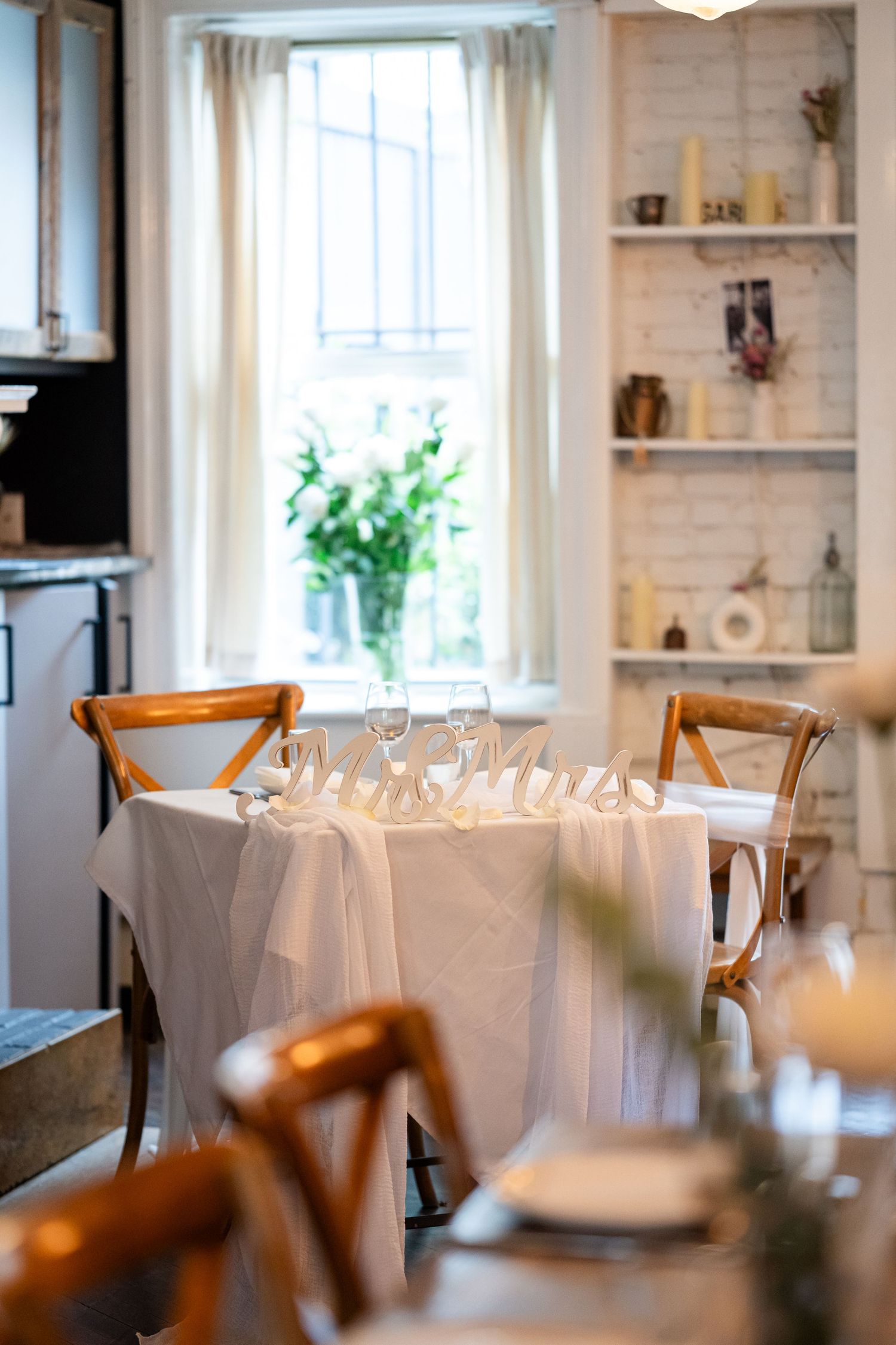 Elegant table setting with white tablecloth and 'Mr & Mrs' sign in a bright dining room.