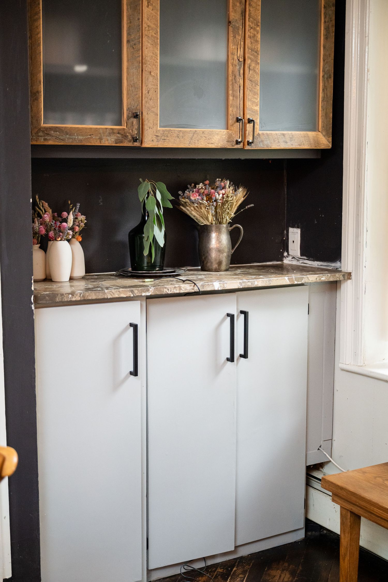 Modern kitchen cabinet with frosted glass doors and dried flower arrangements on marble counter.