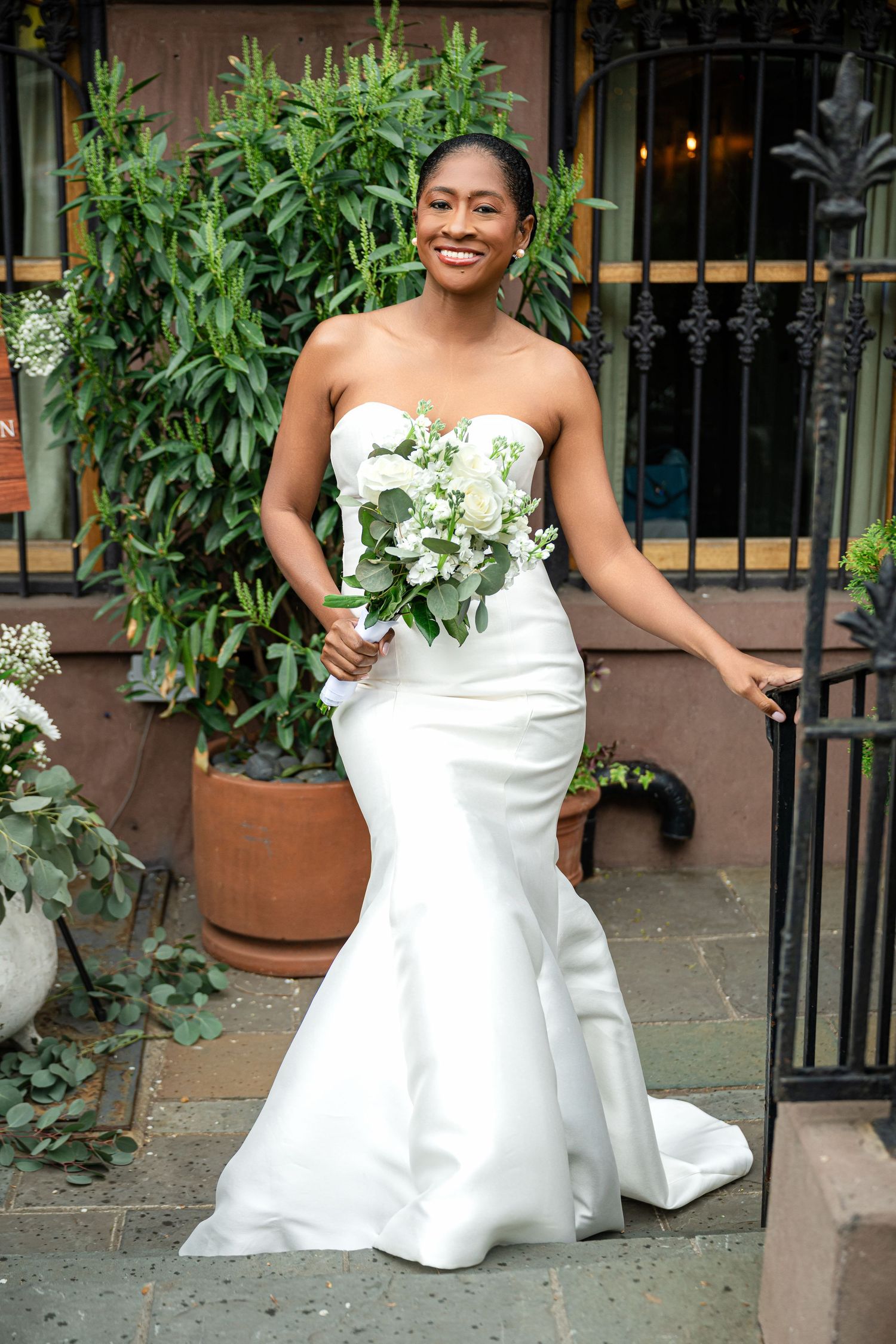 A stunning strapless white wedding gown with a mermaid silhouette and floral bouquet photographed on brownstone steps.