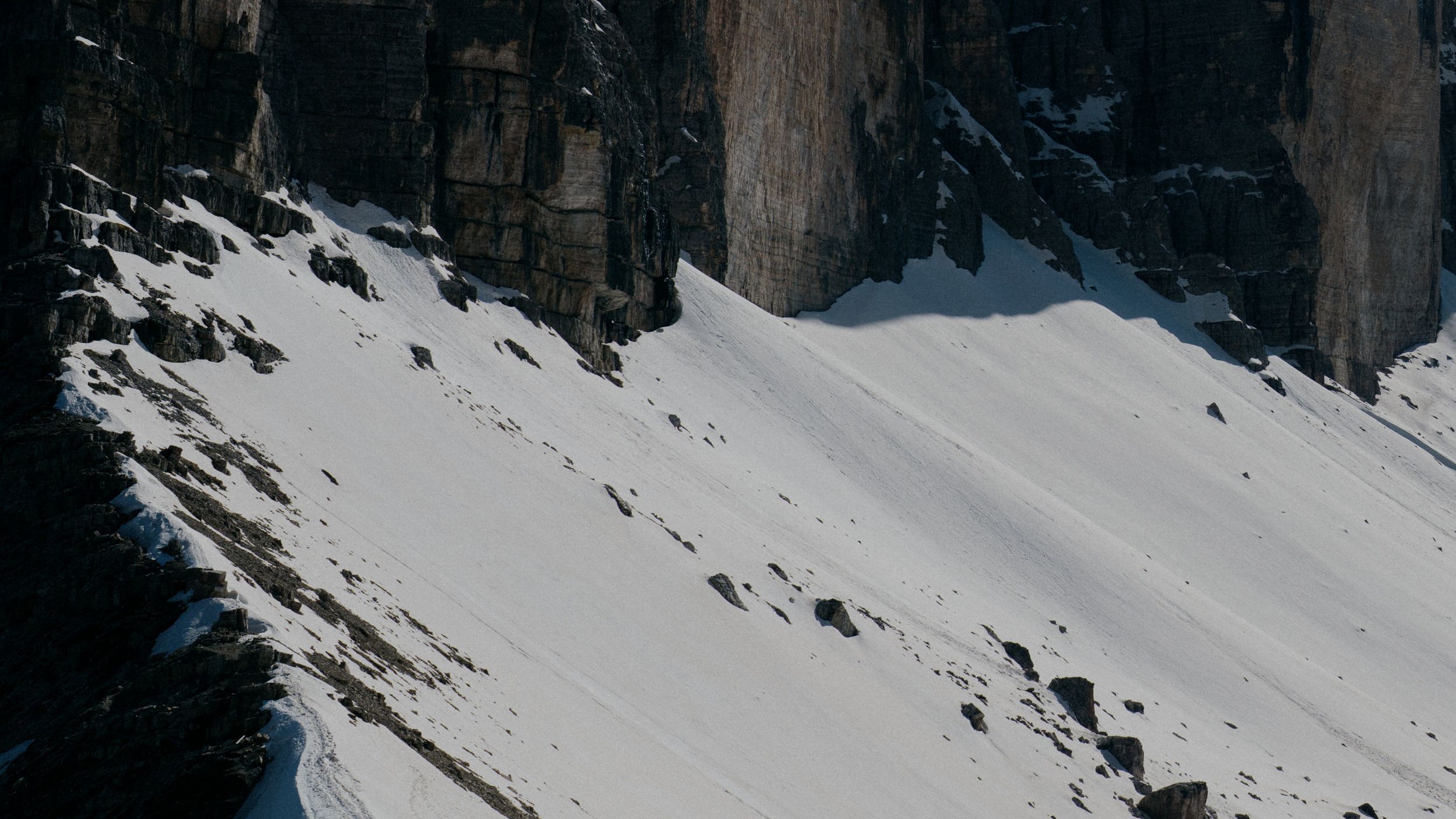 Snow covered mountain slope with jagged rock formations casting dramatic shadows against white powder terrain.