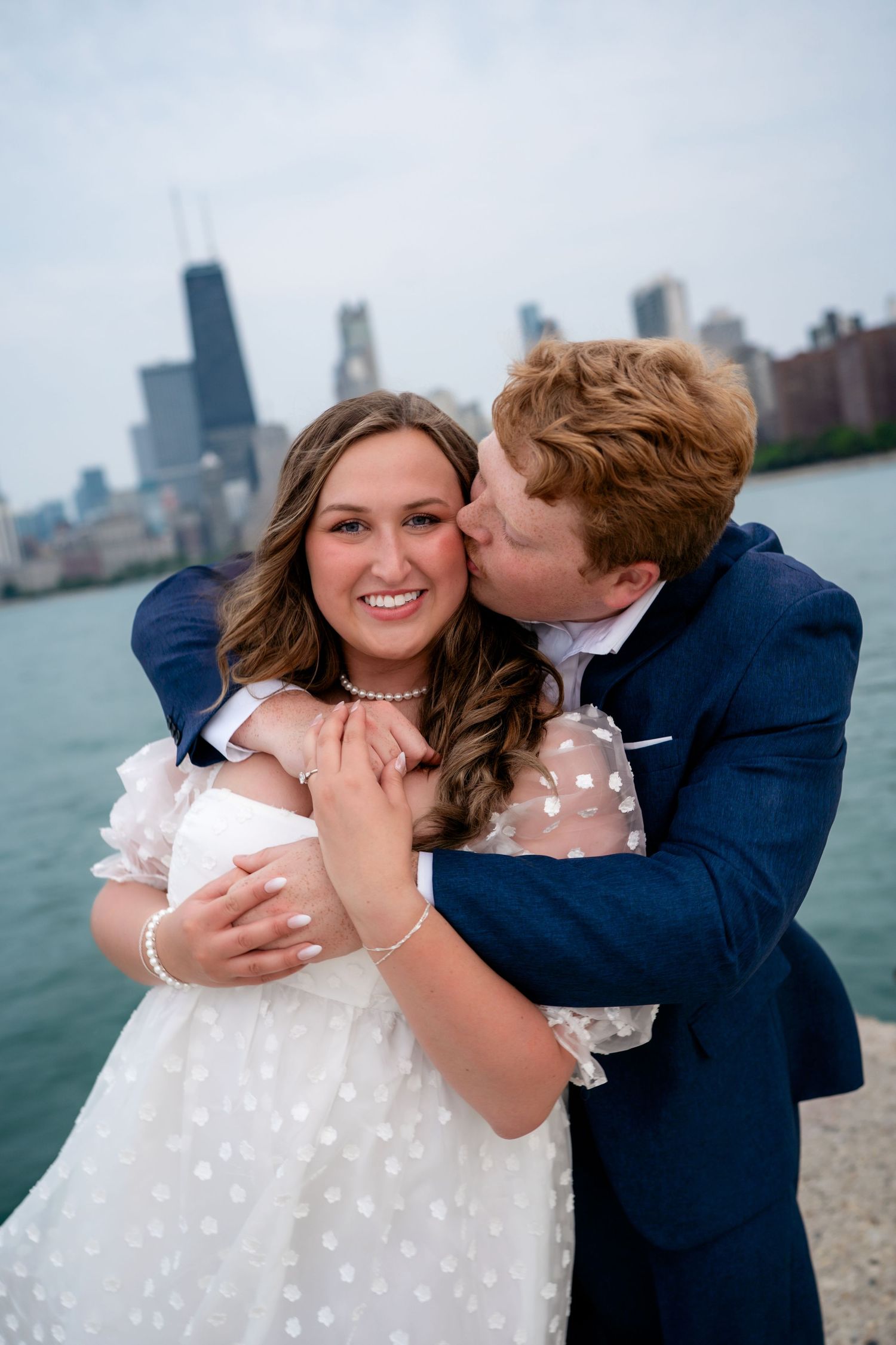 A couple embraces by Lake Michigan with the Chicago skyline in the background.