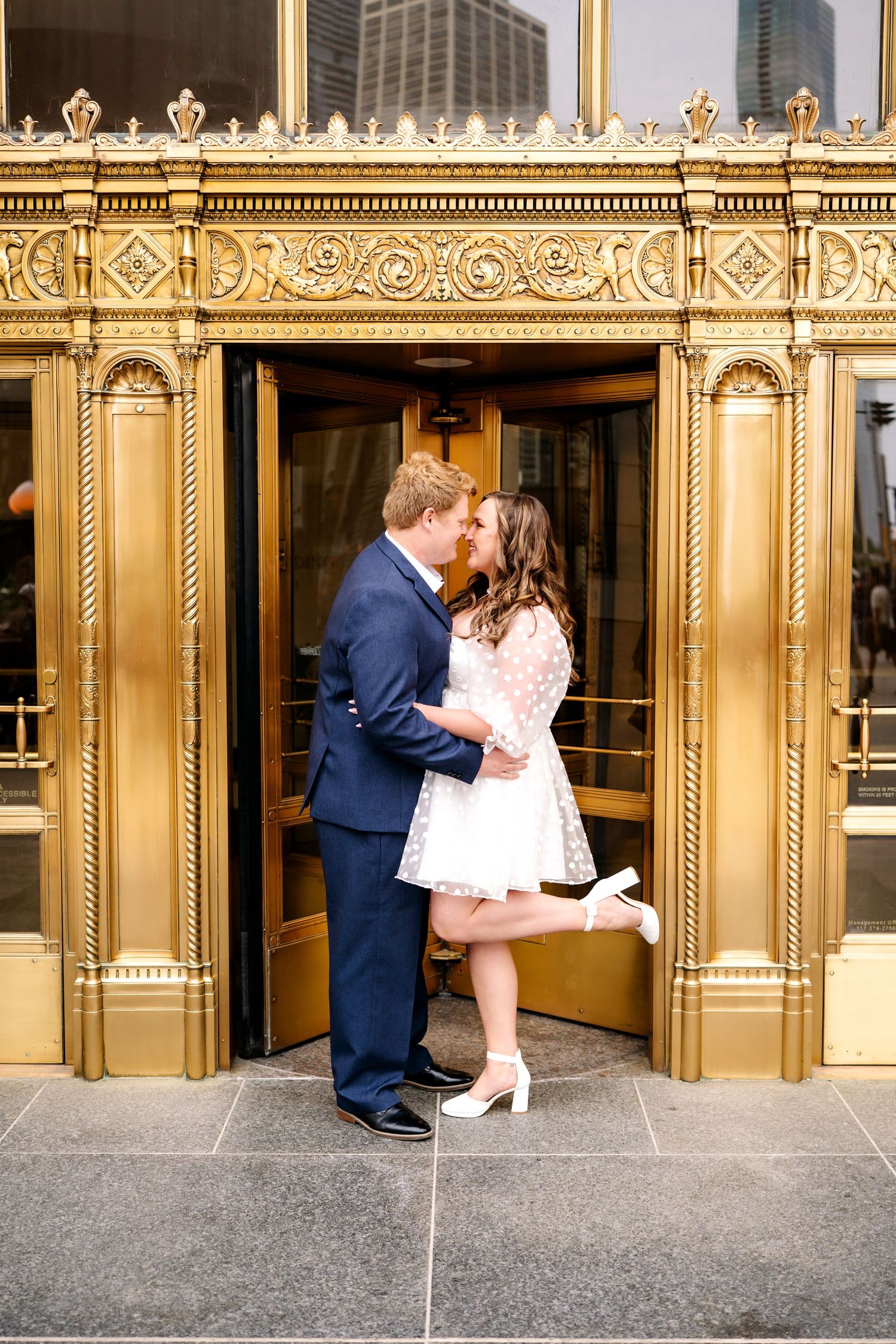 A couple embraces and kisses in front of ornate gold doors in a romantic series of engagement photos.