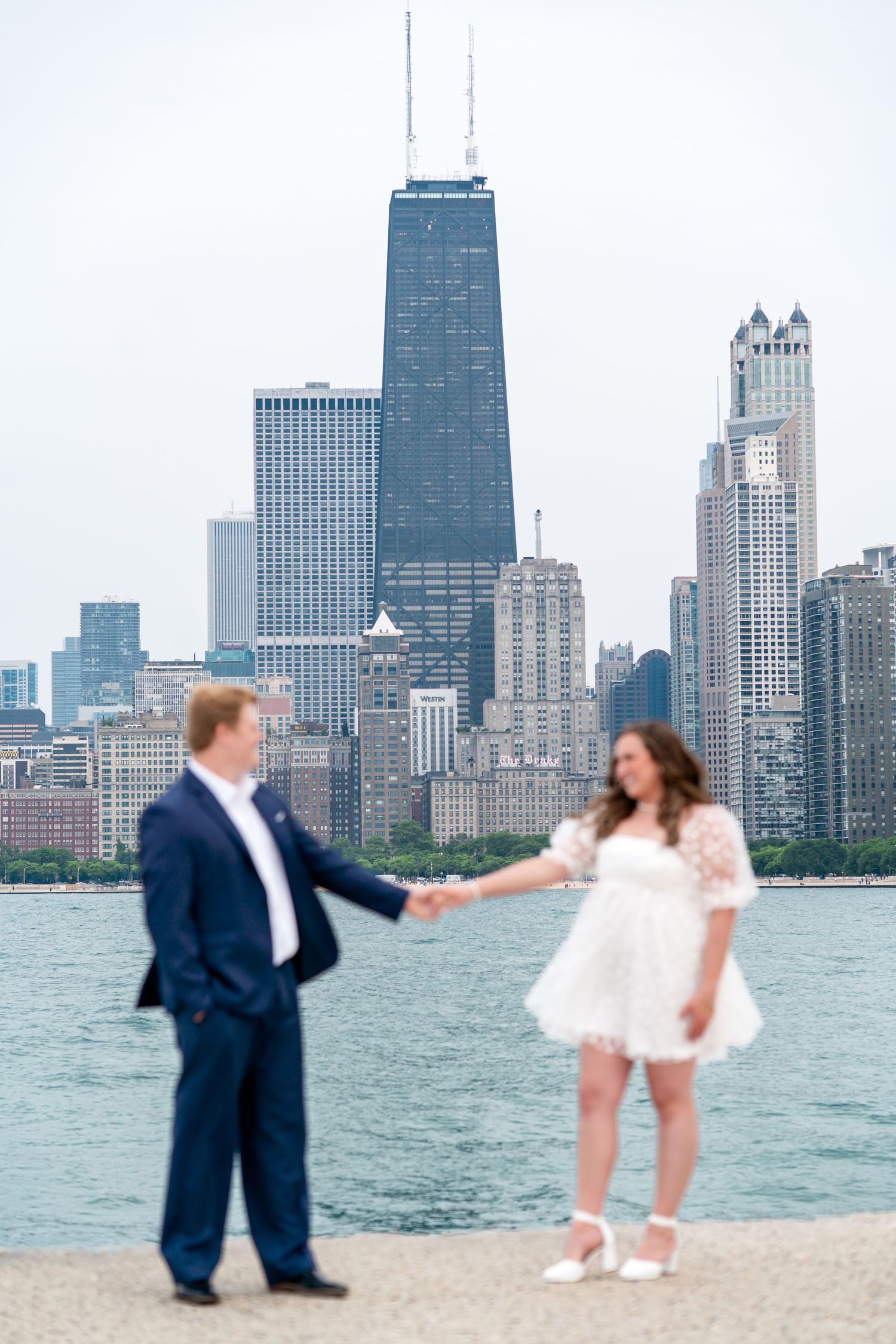 A couple poses along Lake Michigan with the iconic Chicago skyline and John Hancock Center in the background.