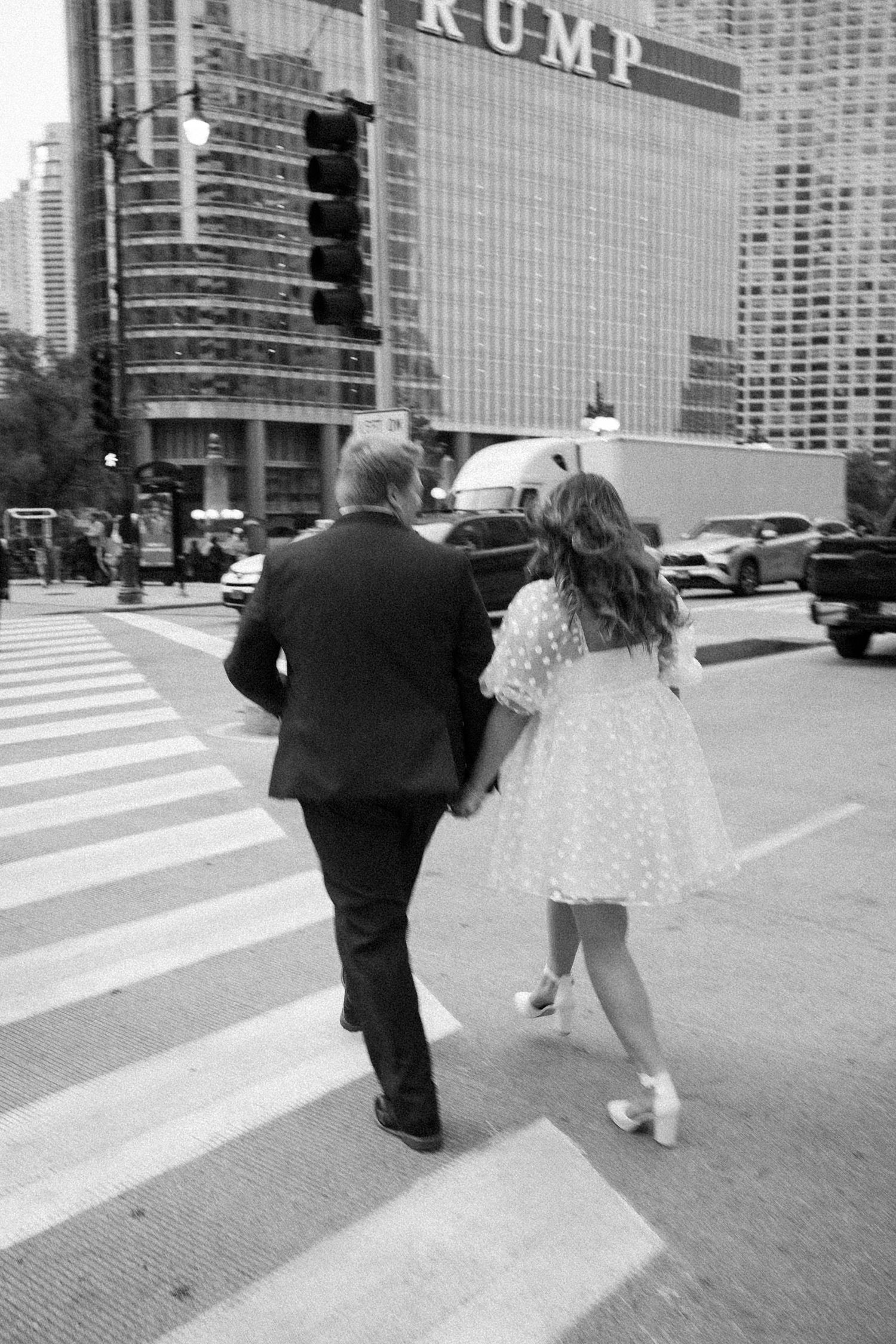 A couple walking across a crosswalk in front of Trump Tower in Chicago's downtown, captured in black and white.
