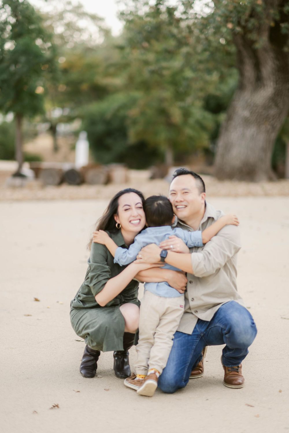 A couple kneels together hugging their small child during a family photo session outdoors.