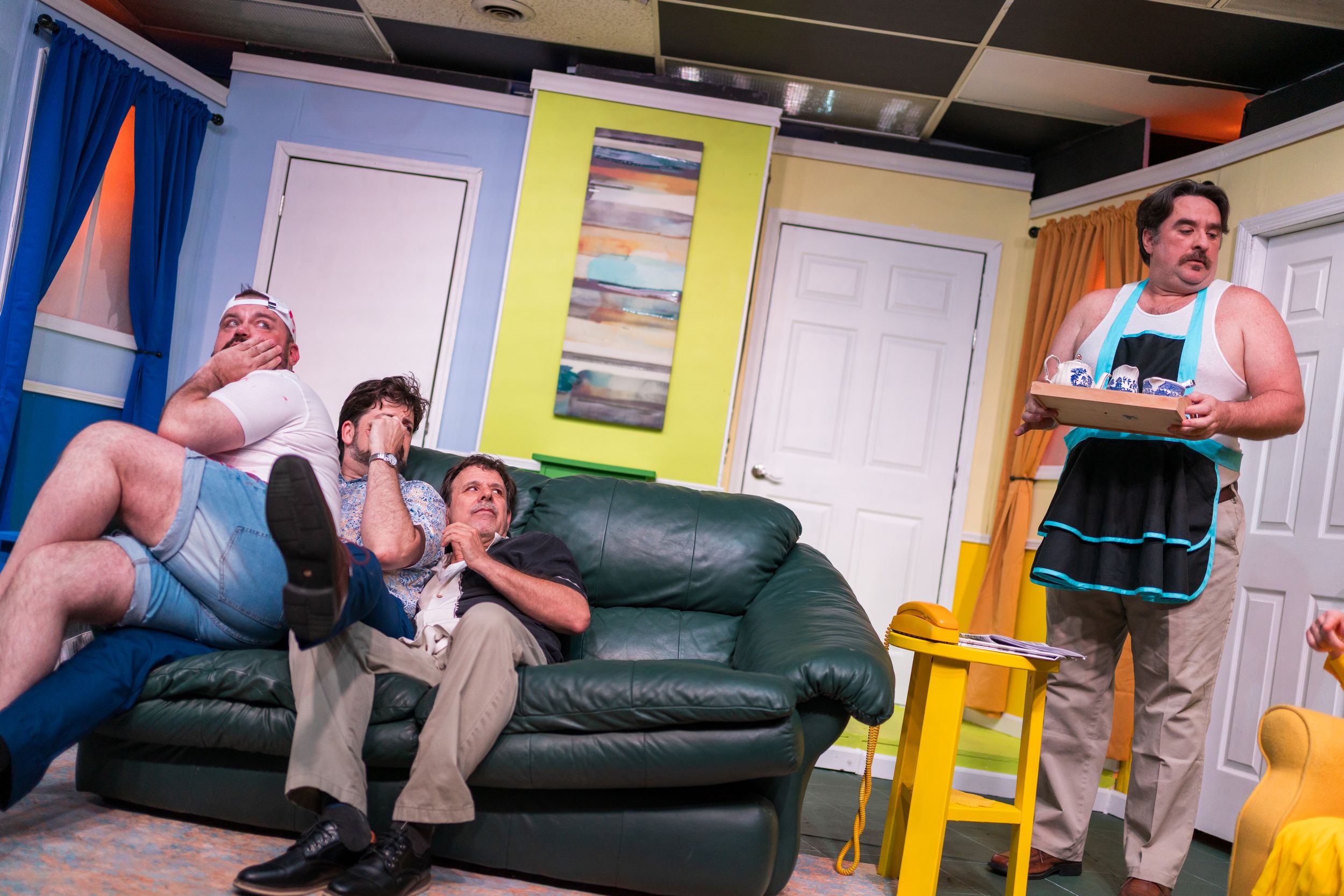 People sitting casually on a green leather couch in a colorful room with blue walls and yellow accents.