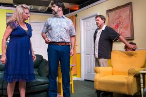 Actors perform an animated scene on stage with a green couch and yellow chair in a colorful living room set.