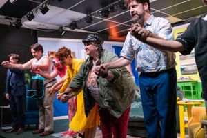 Group performance scene with dramatic lighting and multiple people on stage.