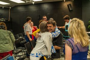 Behind the scenes photo of theater cast and crew members gathering in a rehearsal space.
