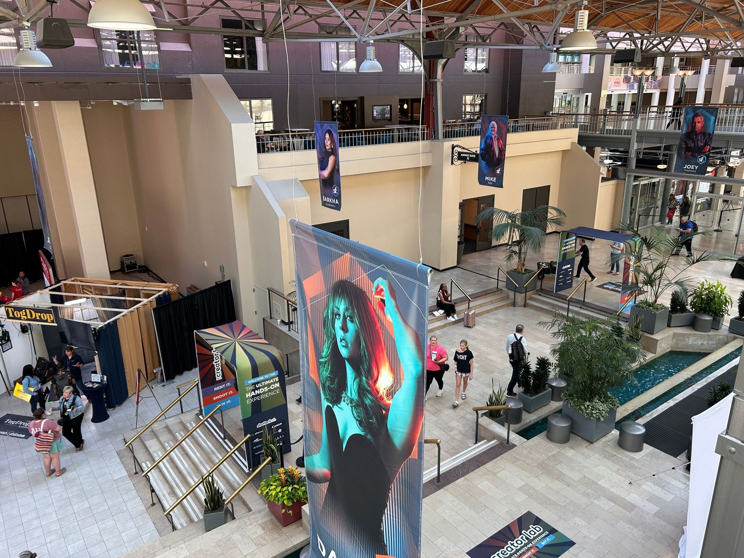 Shoppers browse through a modern indoor shopping center with glass railings and retail storefronts on multiple levels.