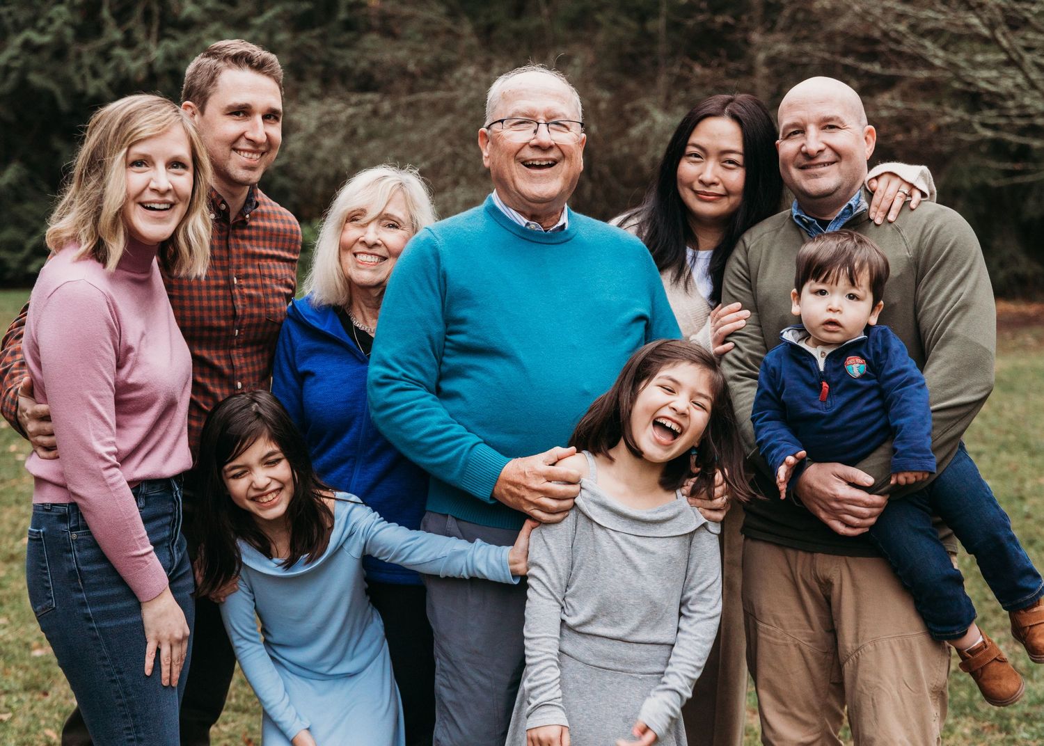 Multi-generation family wearing casual clothing pose together outdoors on an autumn day.