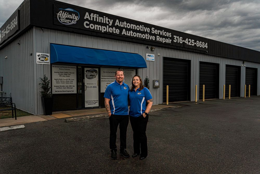 Two automotive service professionals standing in front of Affinity Automotive Services repair shop building.