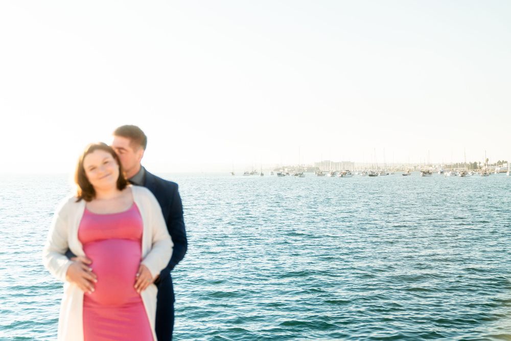 A couple stands together overlooking calm blue ocean waters on a bright sunny day.