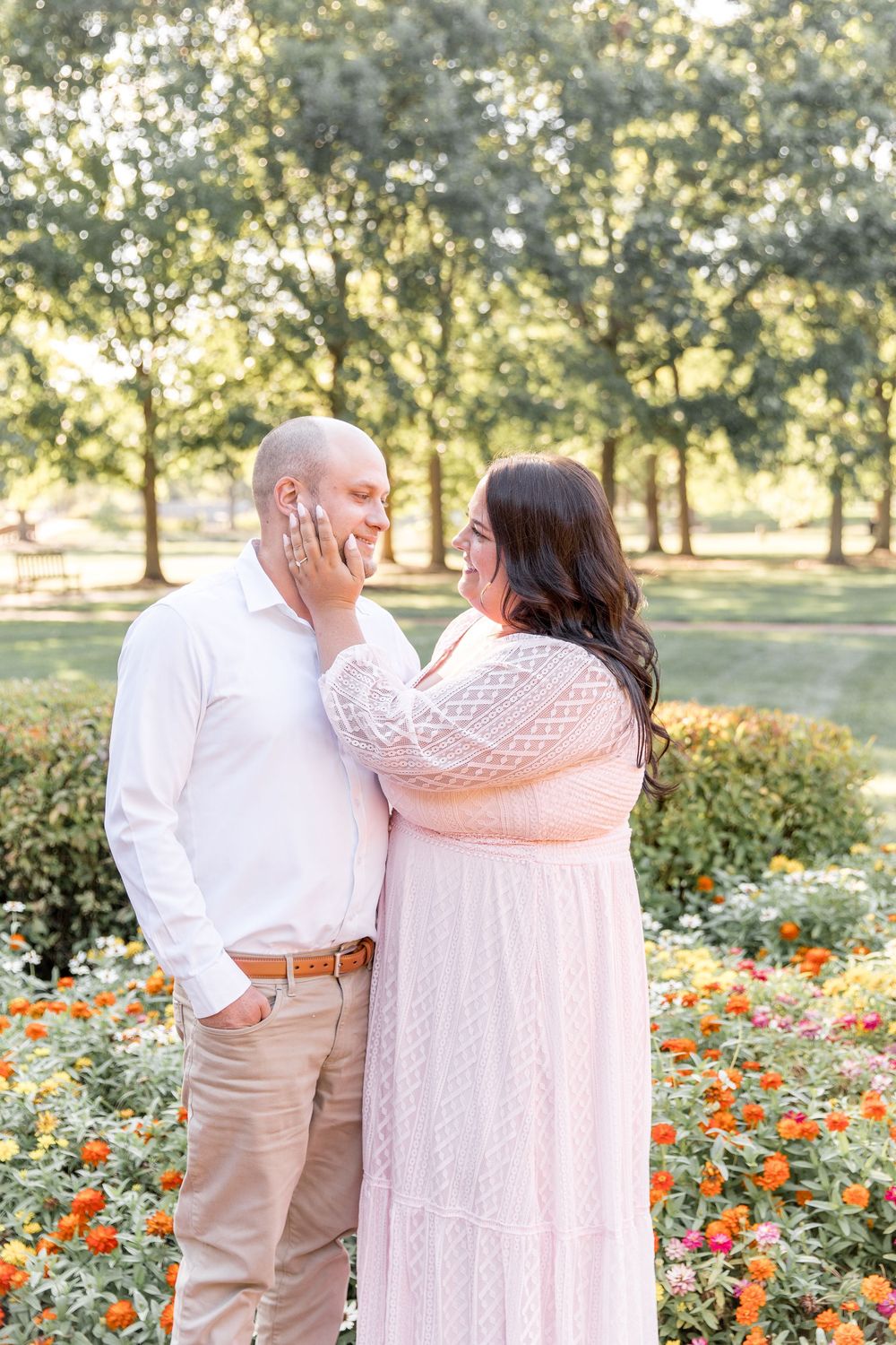A romantic couple shares a tender moment in a garden with blooming orange flowers and trees in the background.