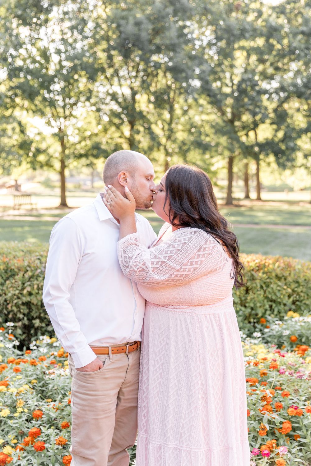 A romantic couple embraces in a garden with blooming orange flowers during a sunny afternoon.