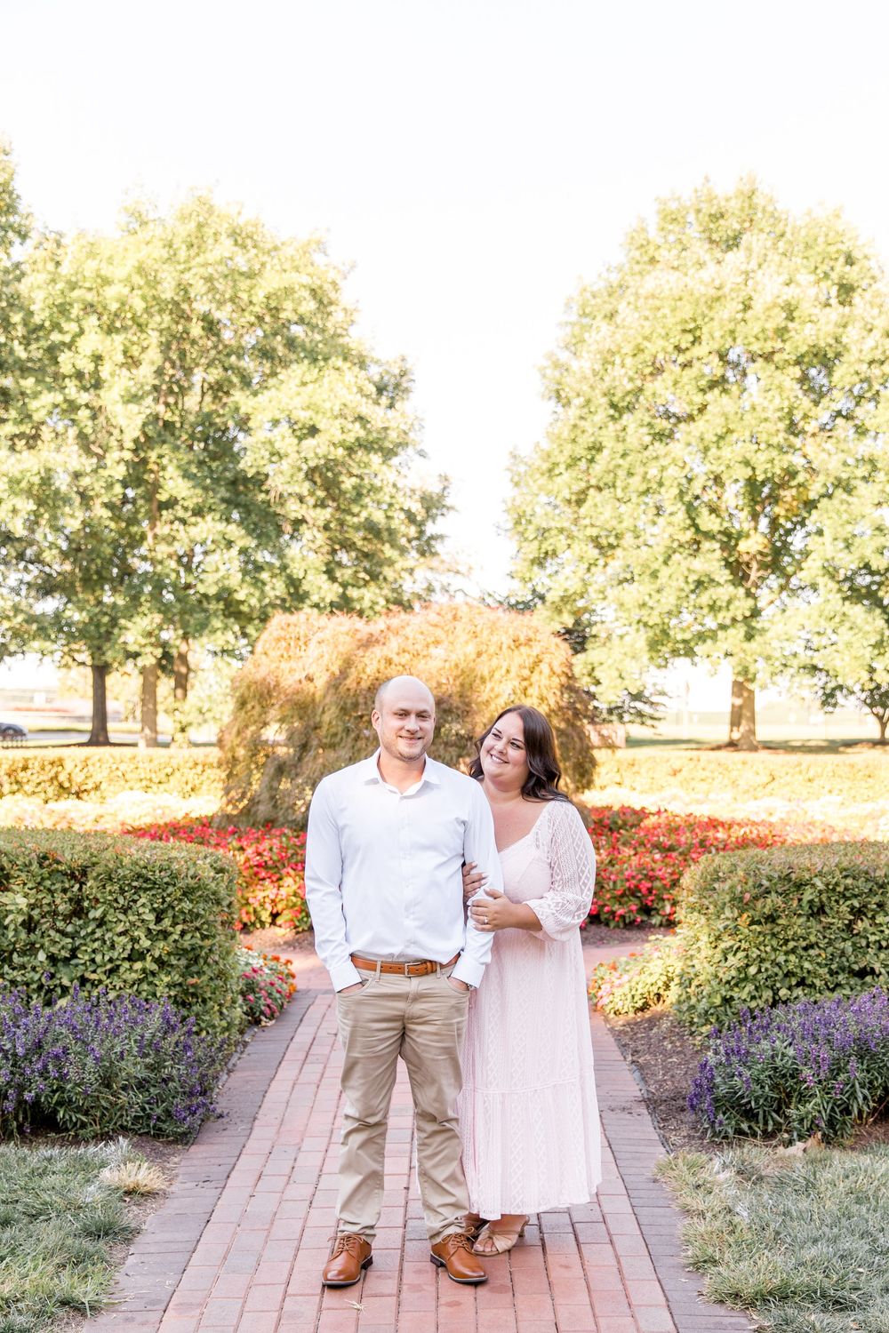 Couple shares a romantic moment on a brick path surrounded by blooming purple flowers and lush greenery.