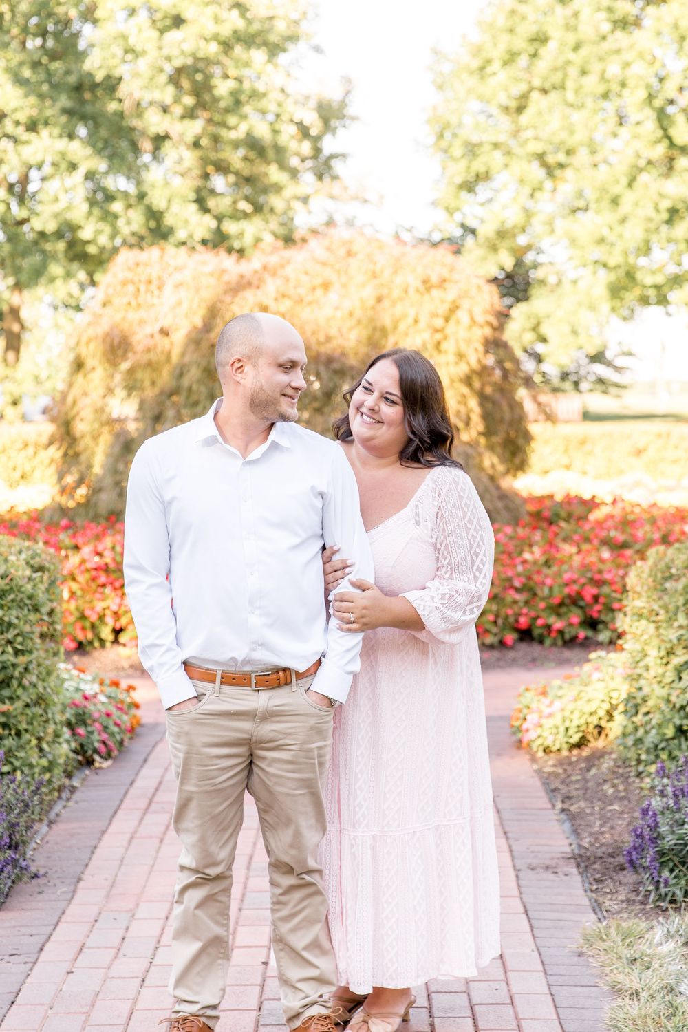 A couple shares a romantic moment in a garden walkway lined with colorful flowers.