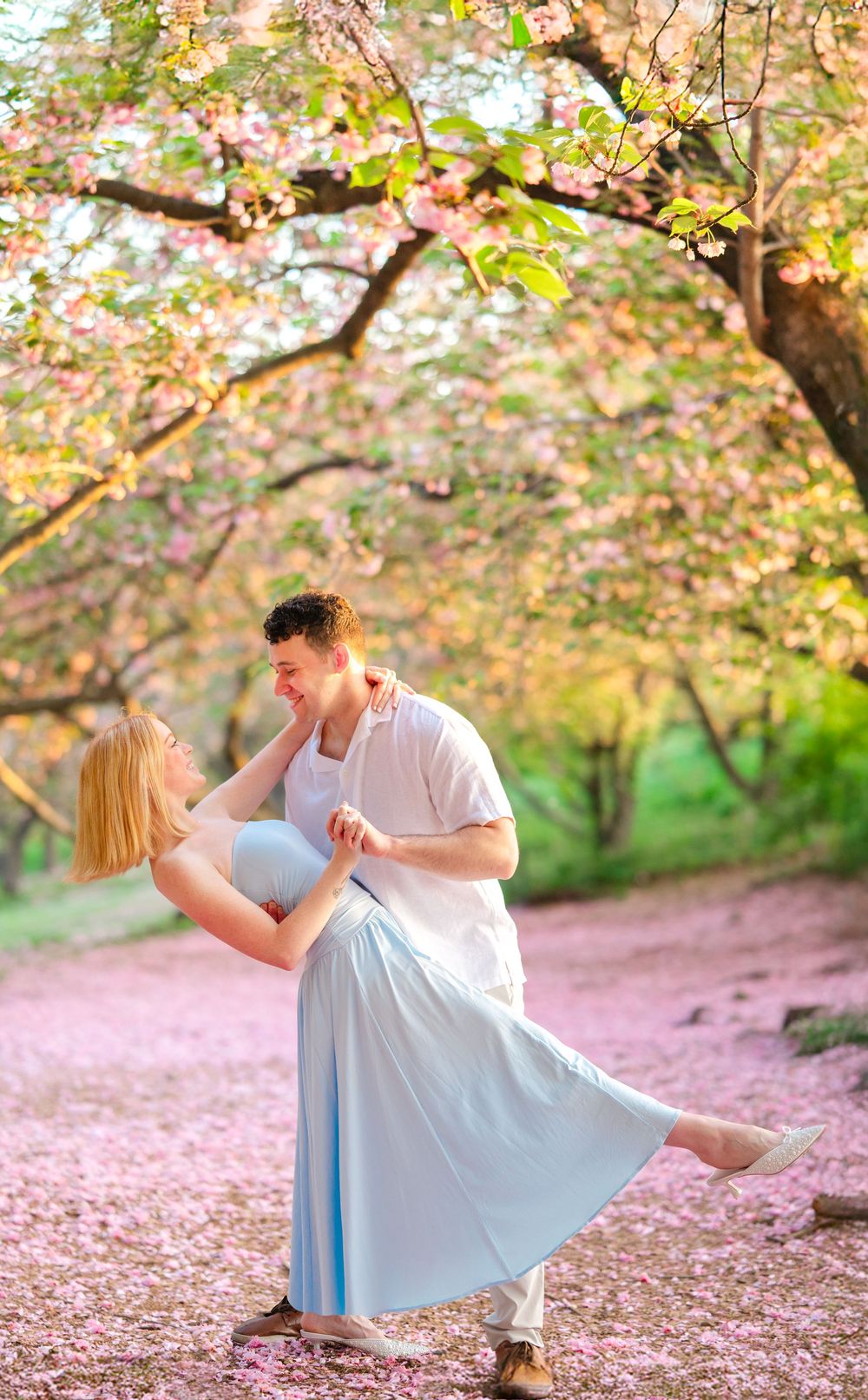 A couple dances romantically beneath pink cherry blossom trees in a spring garden.