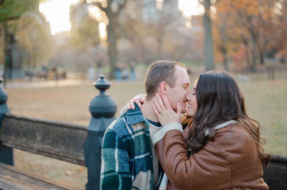 A romantic couple sharing a tender kiss in a park during autumn with fallen leaves in the background.