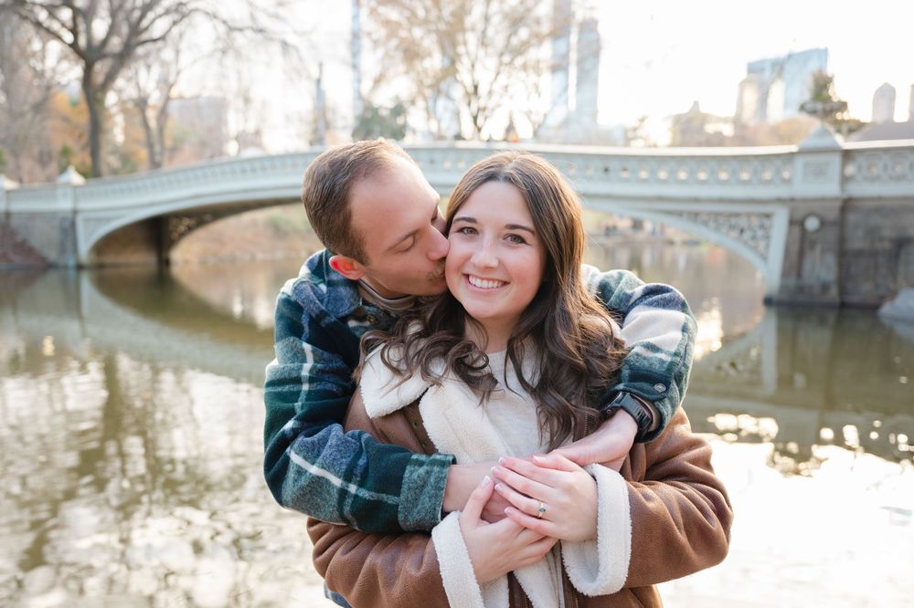 A loving couple embraces near a stone bridge in Central Park on a winter day.