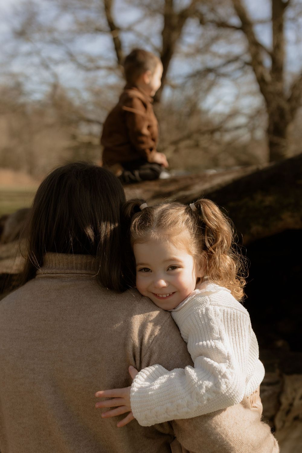 Warm sunlit outdoor scene of someone in a beige sweater holding a child in a white knit sweater during autumn.
