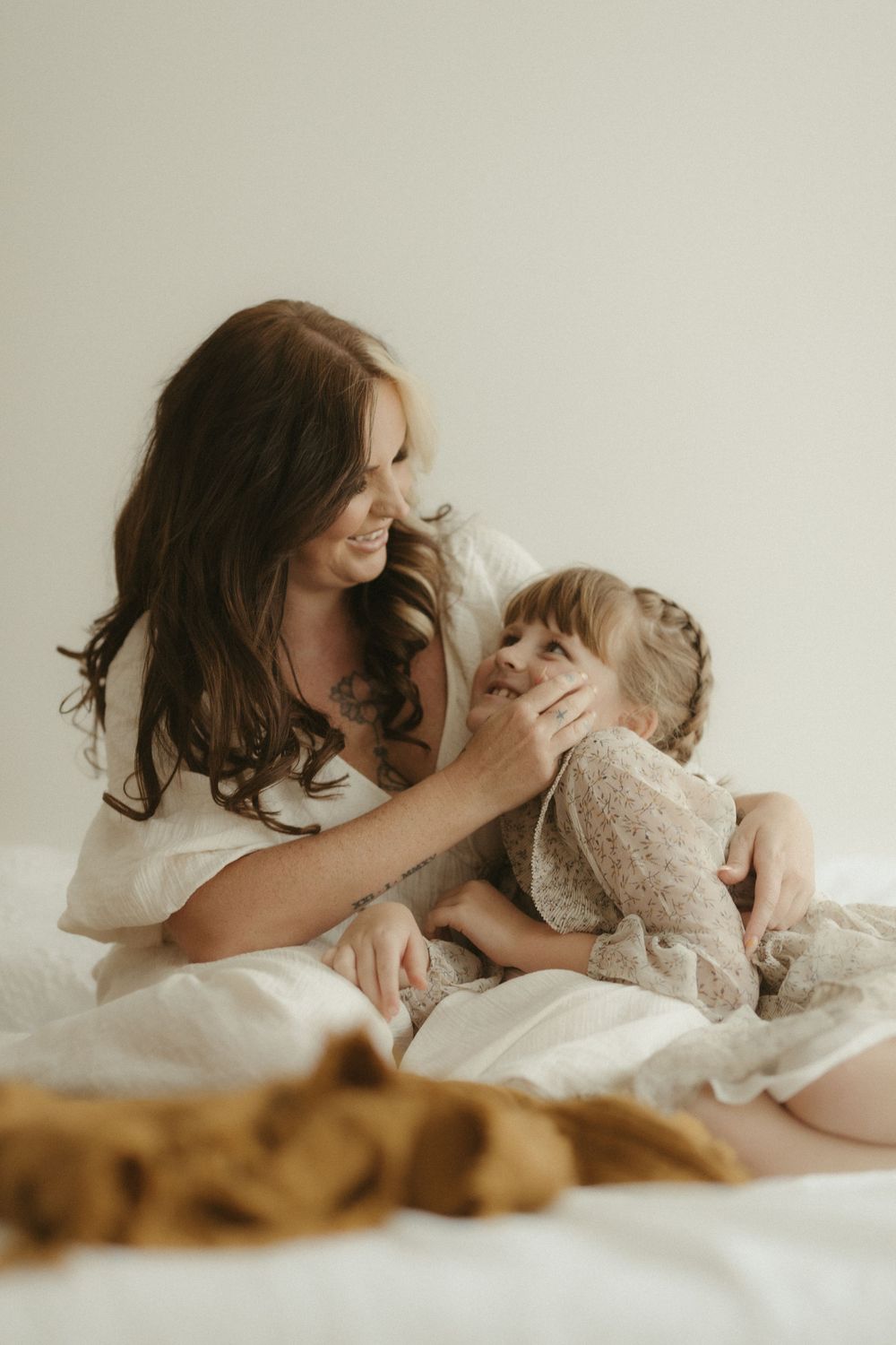 A tender moment between parent and child playing together on white bedding in soft natural light.