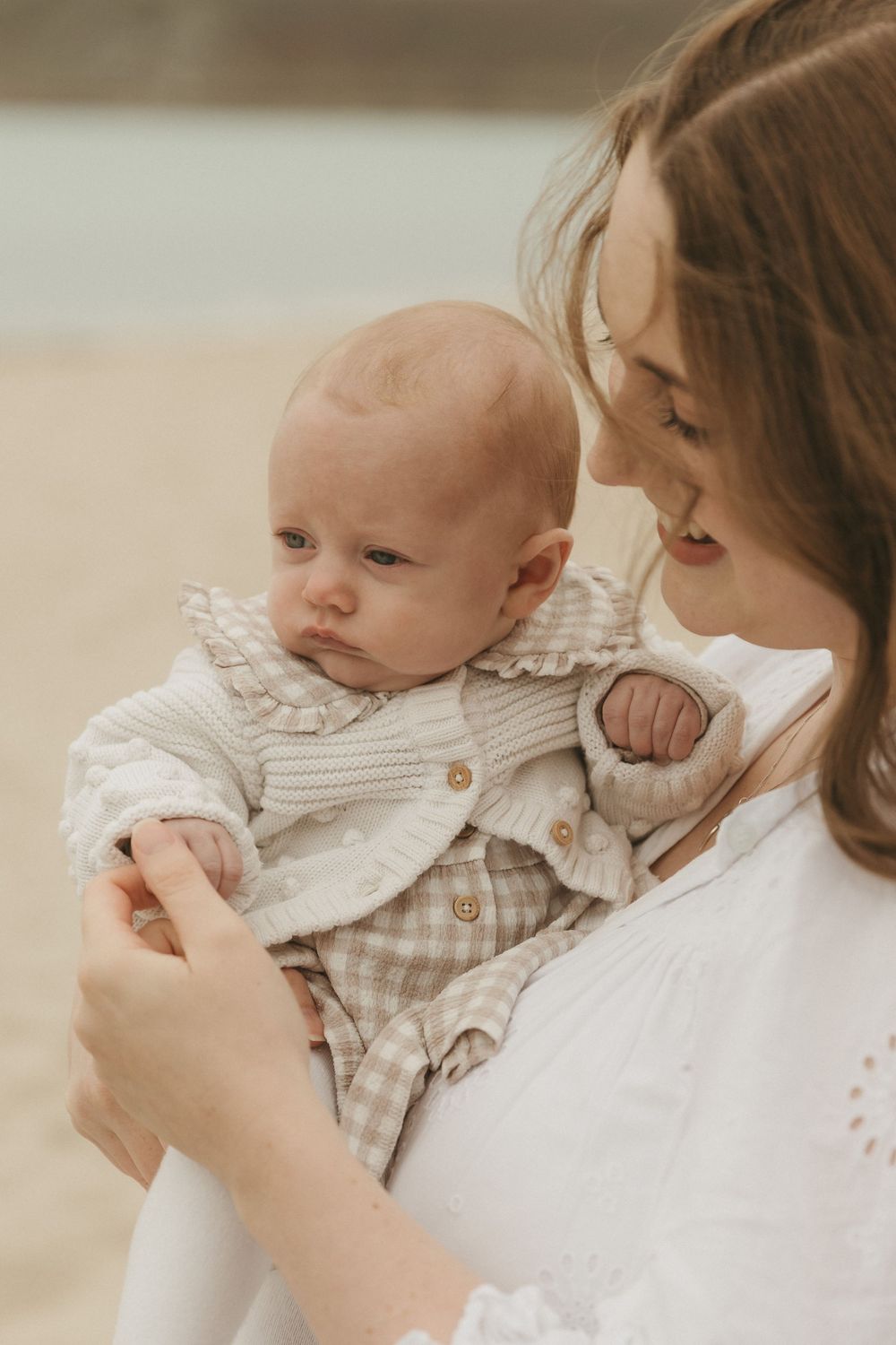 Sweet moment between parent and baby dressed in checkered romper and white knit sweater with warm filtered lighting.