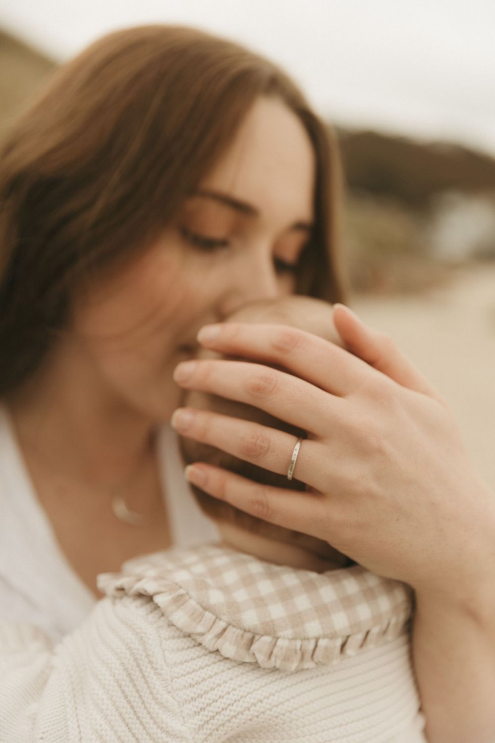Delicate close-up portrait showing hand with engagement ring and cream knit sweater in soft sepia tones.